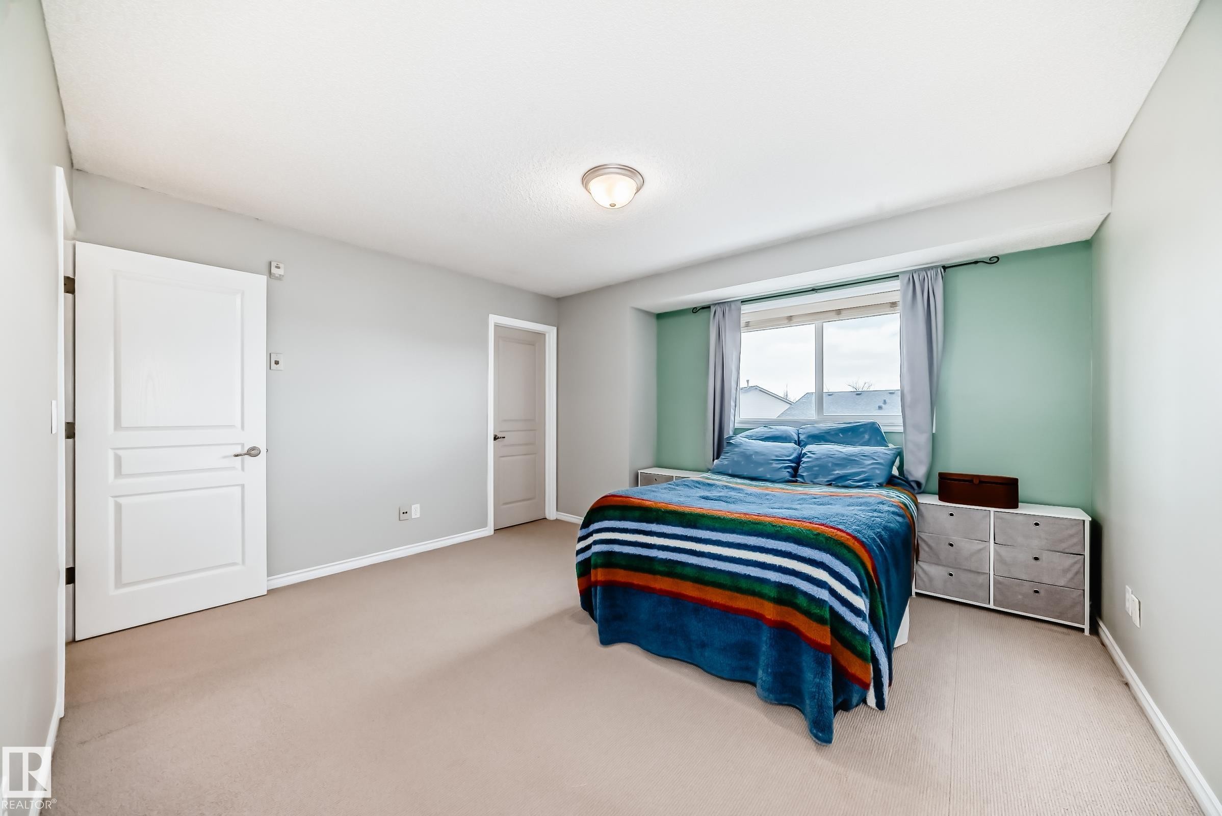 The property features an inviting room with light-colored carpeting, a window providing natural light, and a soft green accent wall - 105 13825 155 Avenue, Edmonton, AB - Indoor Photo Showing Bedroom