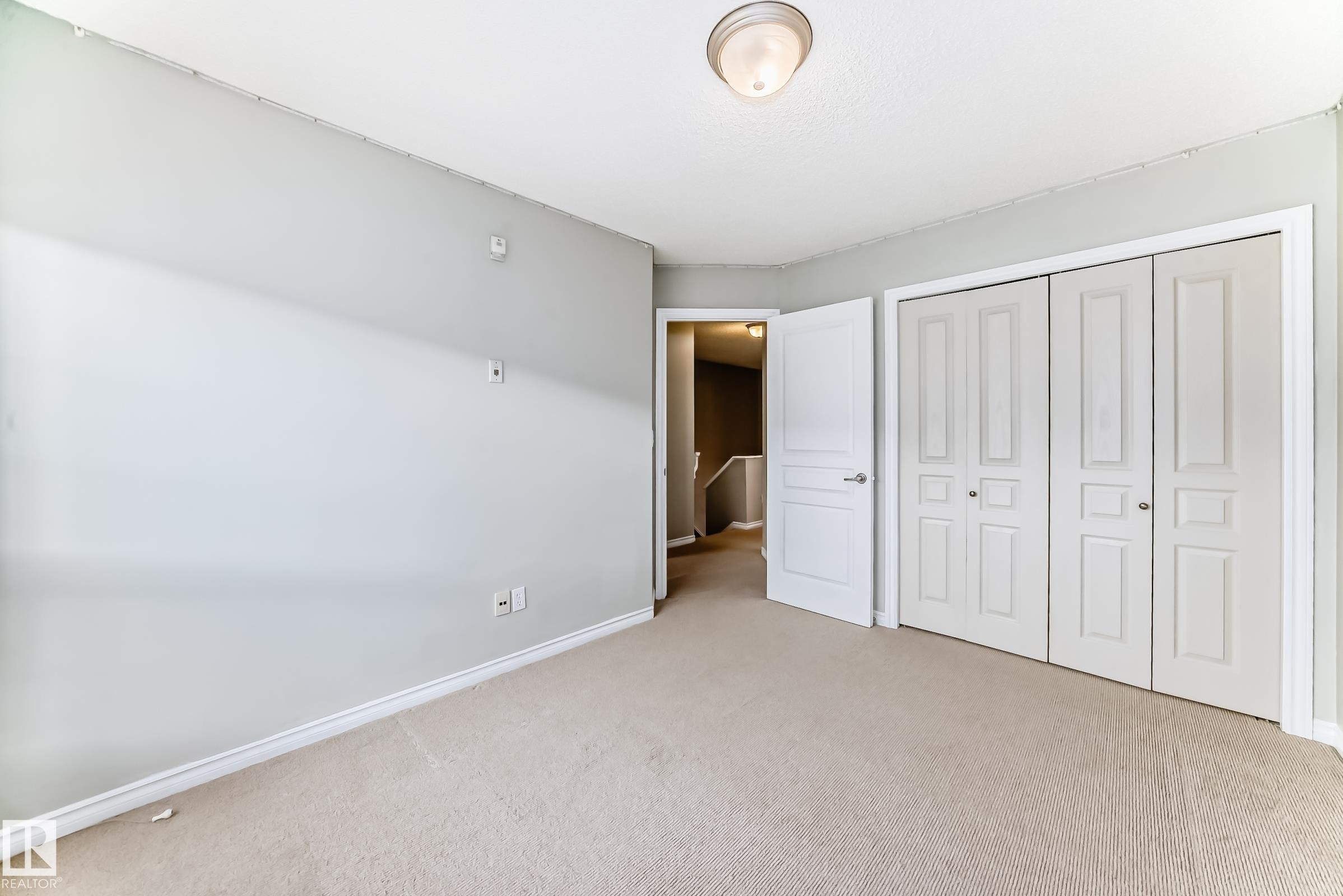 This room features a neutral color palette, carpeted flooring, and a ceiling-mounted light fixture - 105 13825 155 Avenue, Edmonton, AB - Indoor