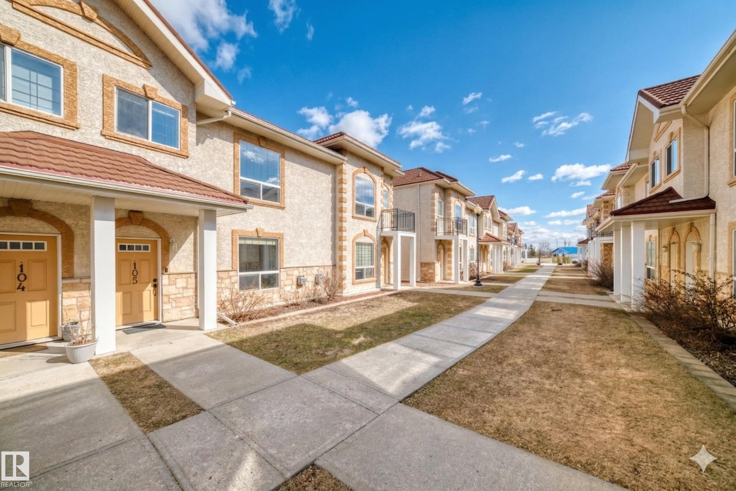 The property features a stucco exterior with stone accents, a red tile roof, and individual front entrances with transom windows - 105 13825 155 Avenue, Edmonton, AB - Outdoor