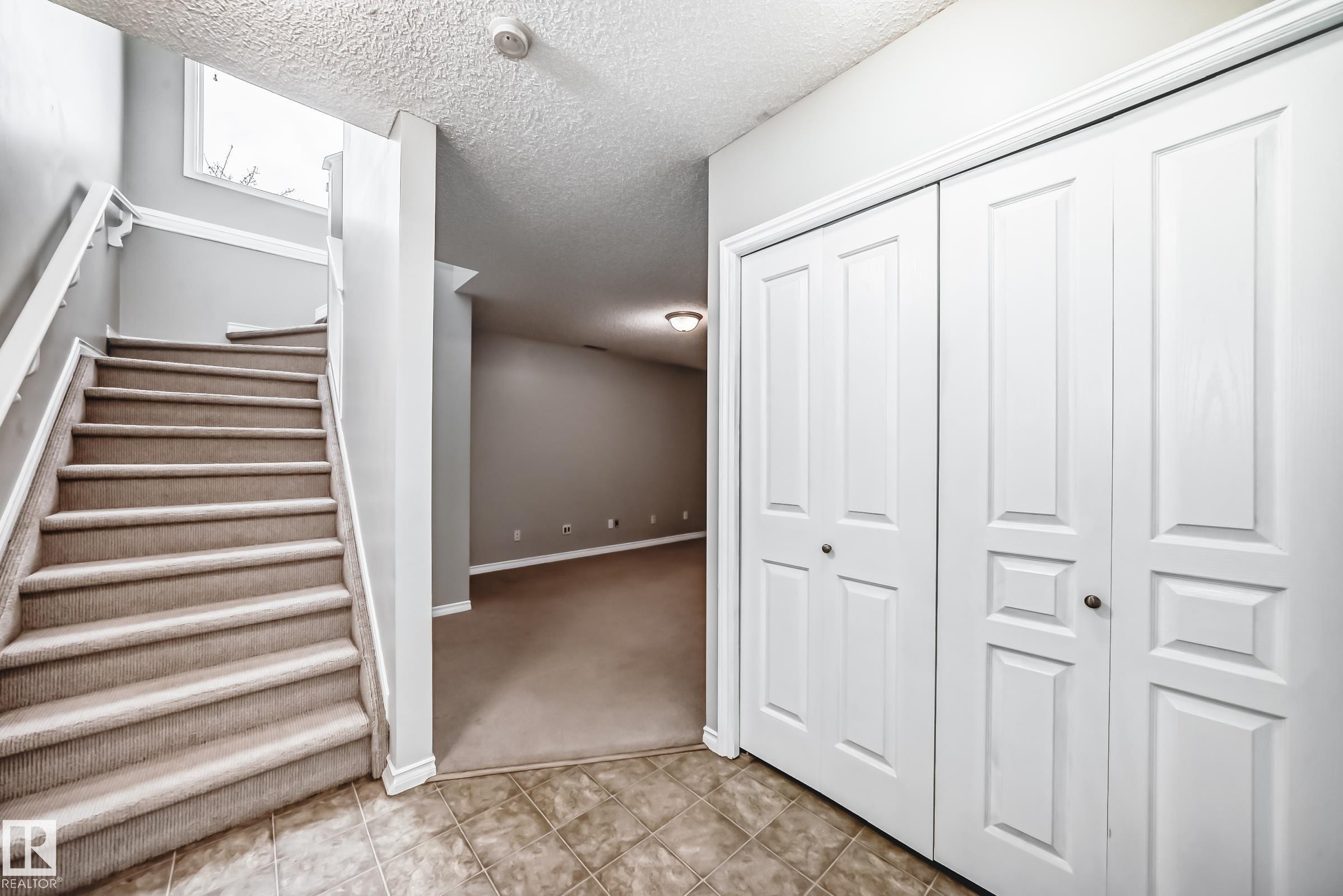 The property features a staircase with carpeted treads and white handrails, a storage closet with bi-fold doors, and a tiled entryway - 105 13825 155 Avenue, Edmonton, AB - Indoor Photo Showing Other Room