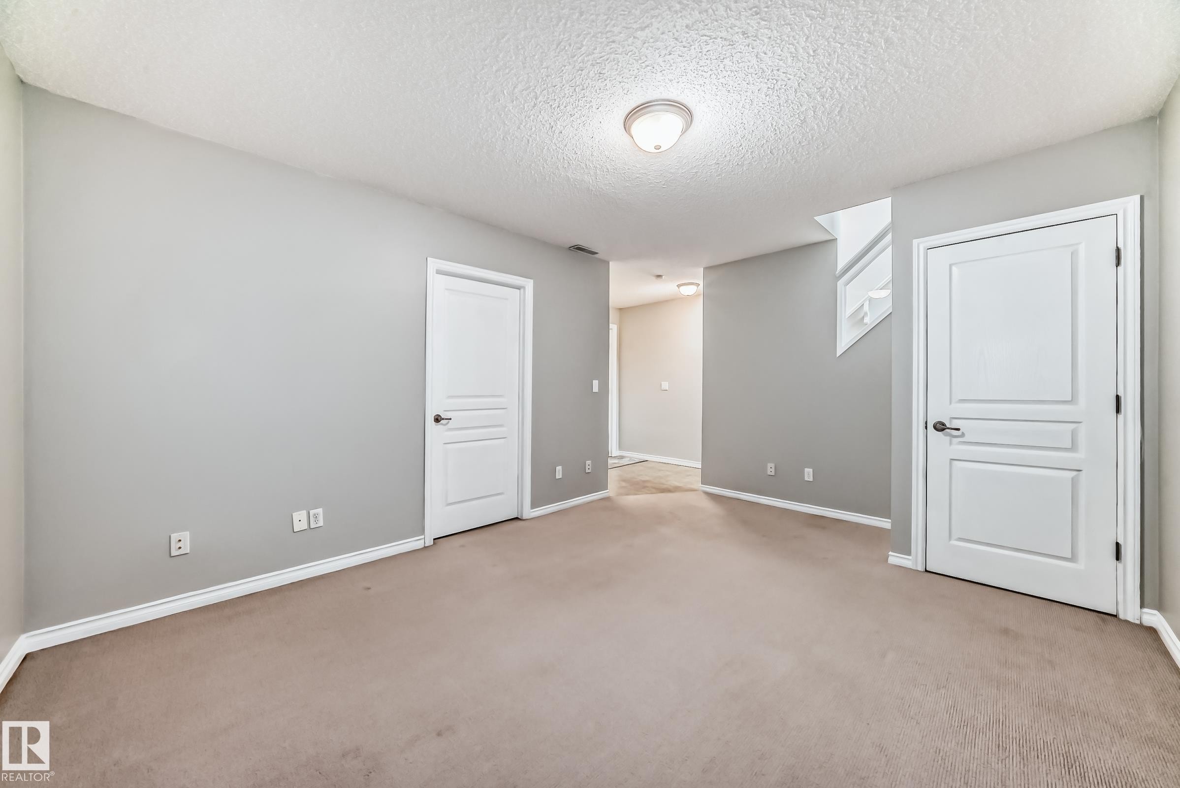 An open room with light grey walls, white trim, and light brown carpeting - 105 13825 155 Avenue, Edmonton, AB - Indoor Photo Showing Other Room