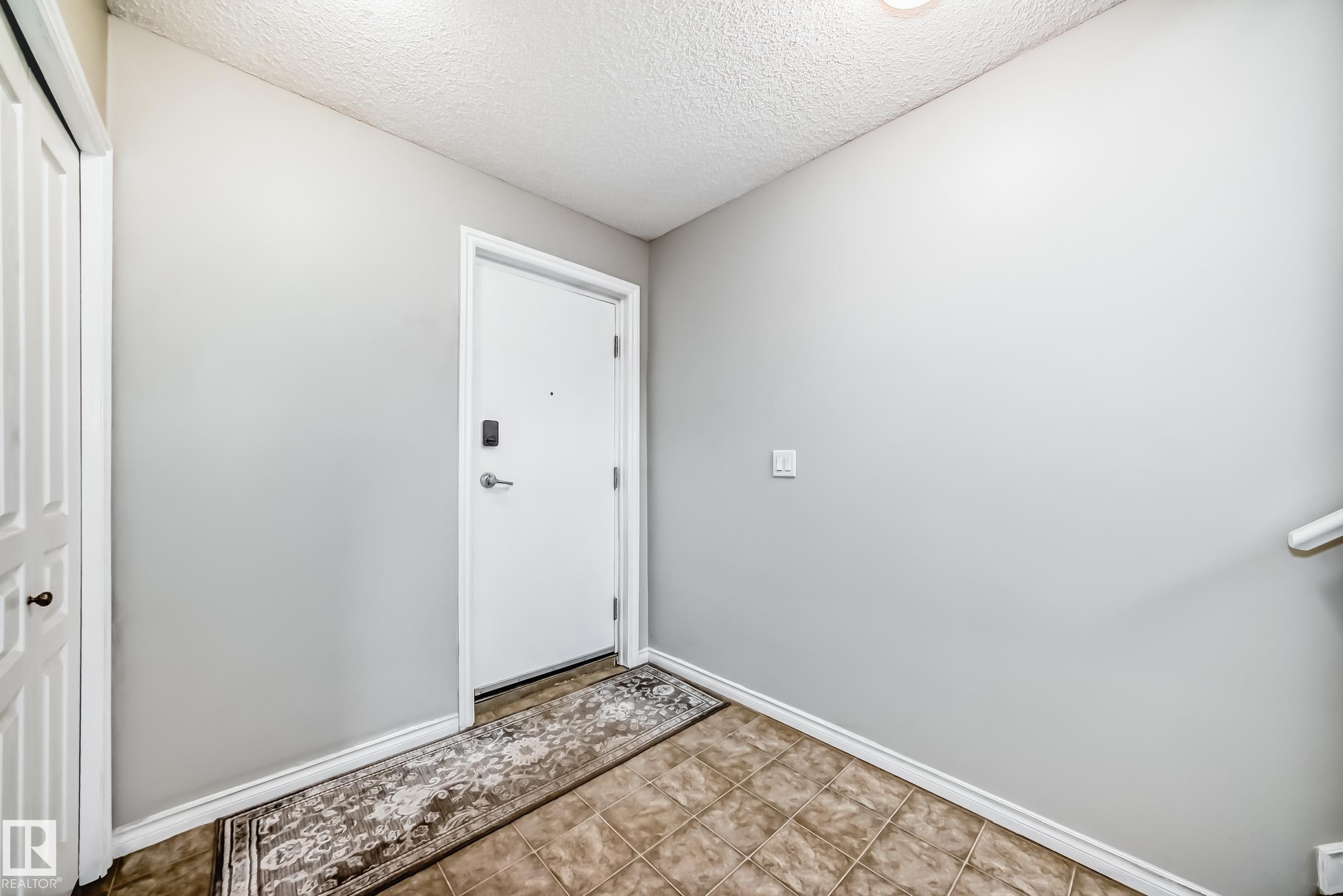 The property features a white entry door with a digital lock, light grey walls, and a tiled floor - 105 13825 155 Avenue, Edmonton, AB - Indoor Photo Showing Other Room