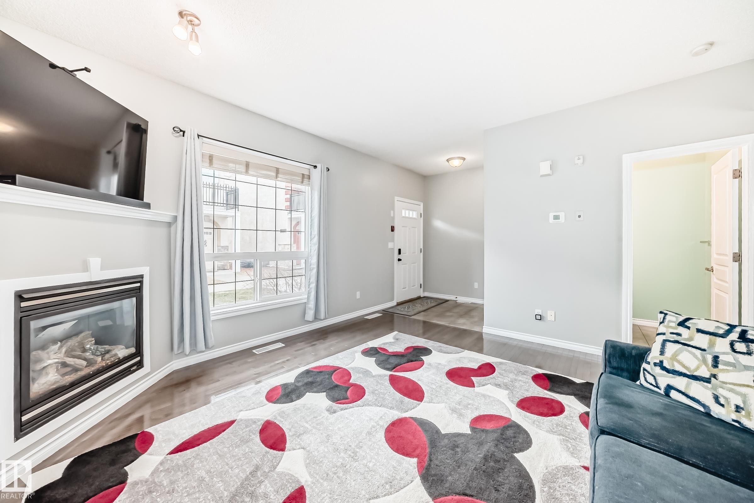 The living area features light gray walls, hardwood flooring, and a large window providing ample natural light - 105 13825 155 Avenue, Edmonton, AB - Indoor With Fireplace
