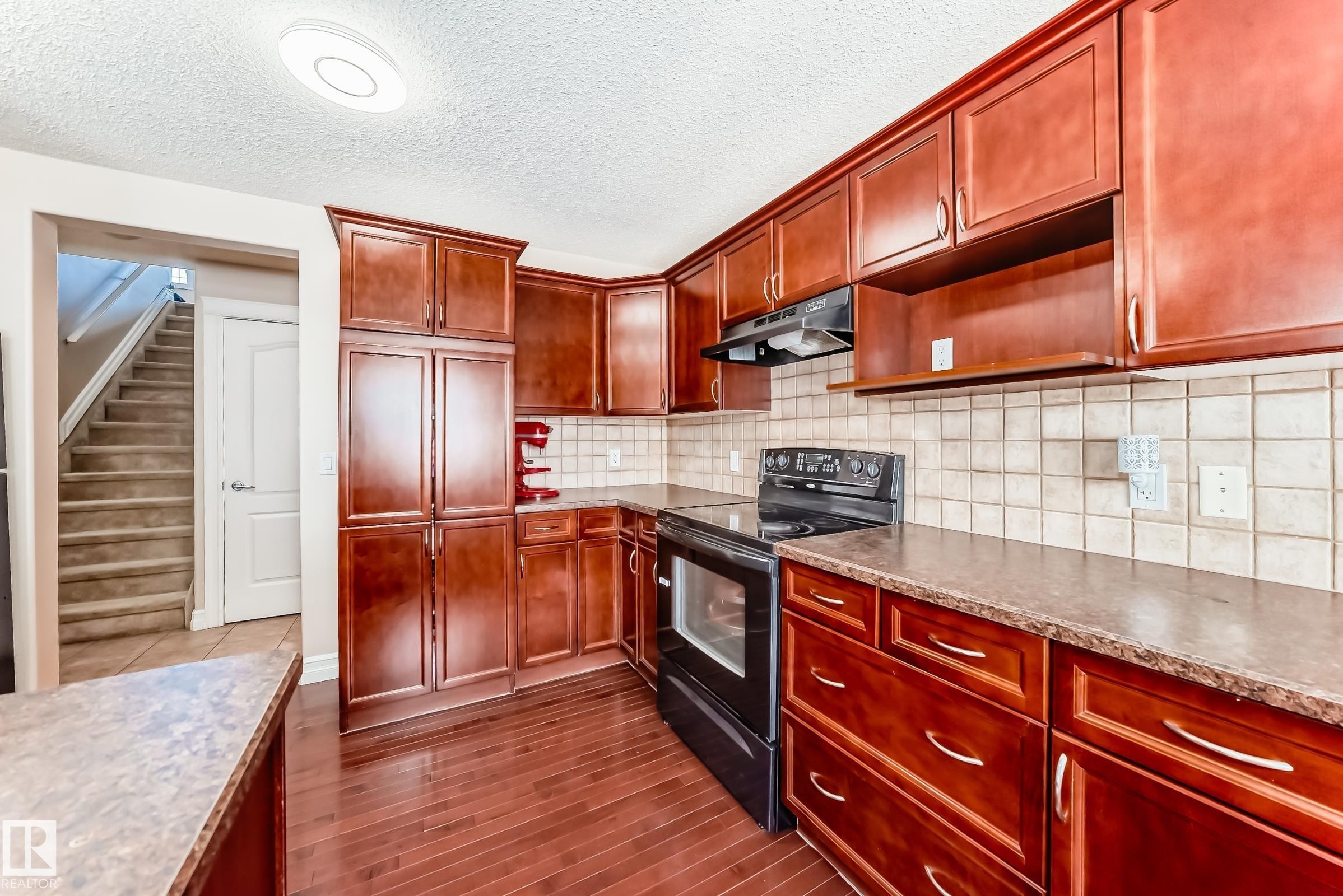 The kitchen features rich wood cabinetry, a tiled backsplash, and dark countertops - 11415 167A Avenue Nw, Edmonton, AB - Indoor Photo Showing Kitchen