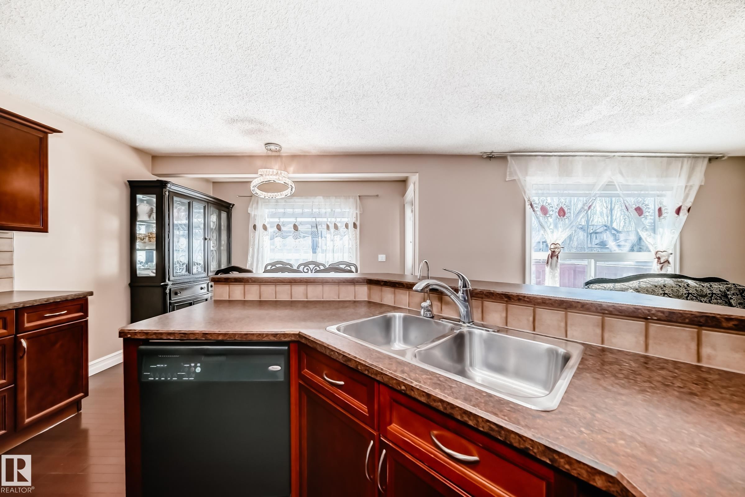 The kitchen features a stainless steel double basin sink with a chrome faucet, dark wood cabinetry, and a black dishwasher - 11415 167A Avenue Nw, Edmonton, AB - Indoor Photo Showing Kitchen With Double Sink