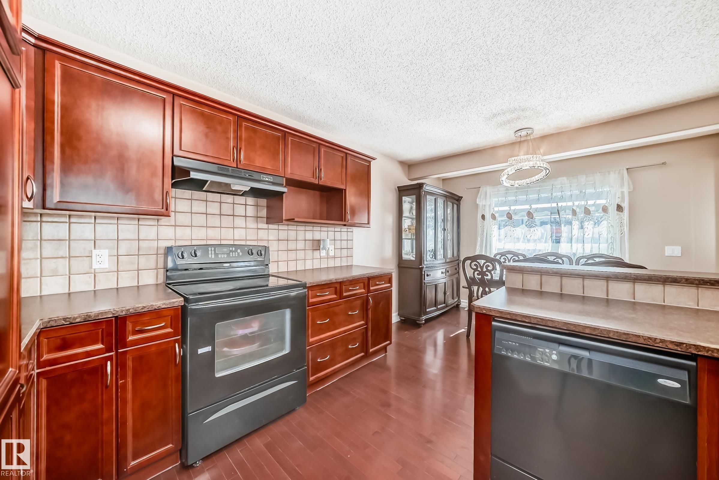 The kitchen features rich wood cabinetry, a tiled backsplash, and a black range with an overhead exhaust fan - 11415 167A Avenue Nw, Edmonton, AB - Indoor Photo Showing Kitchen