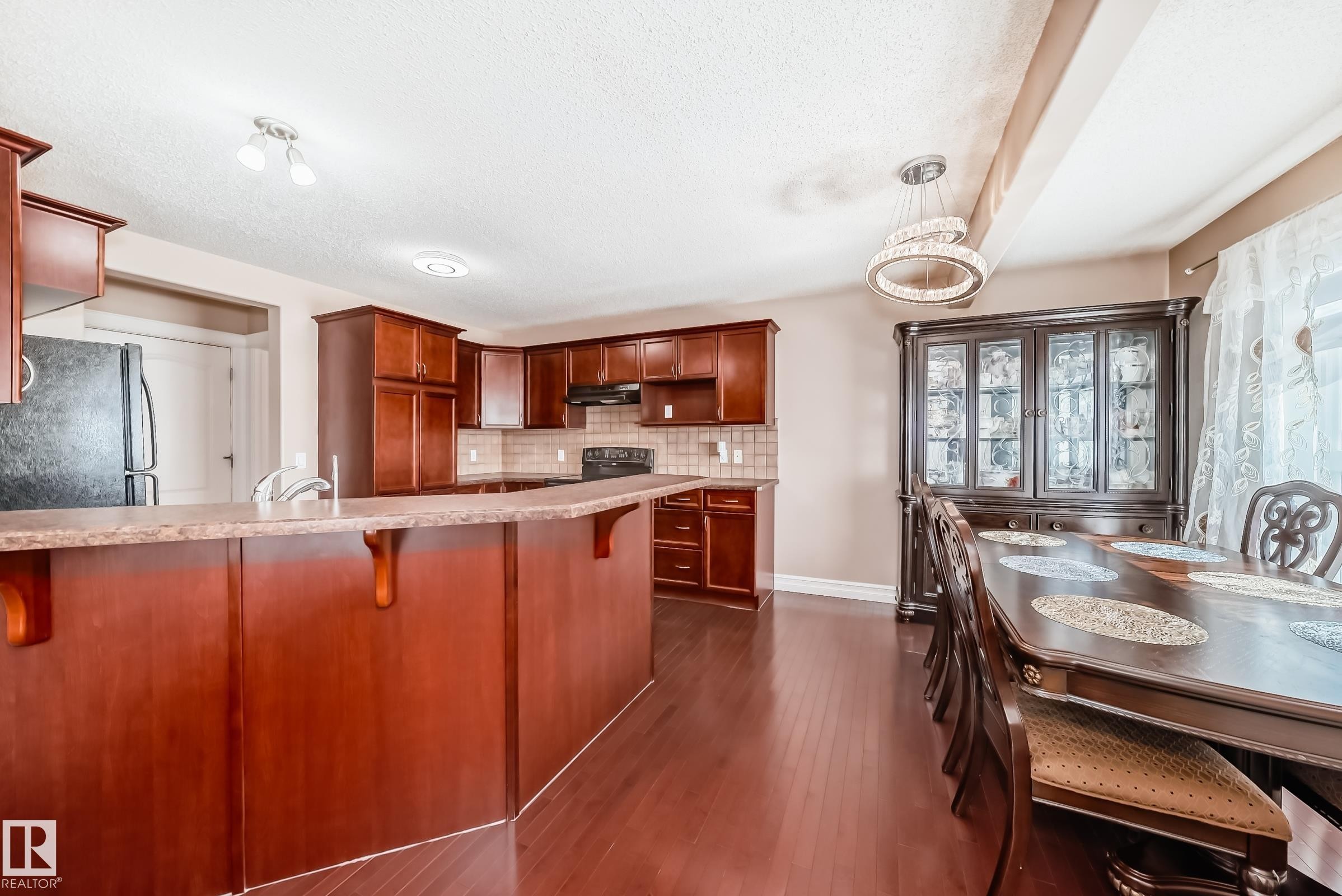 This kitchen and dining area features rich wood cabinetry, a breakfast bar with a speckled countertop, and dark wood flooring - 11415 167A Avenue Nw, Edmonton, AB - Indoor Photo Showing Kitchen