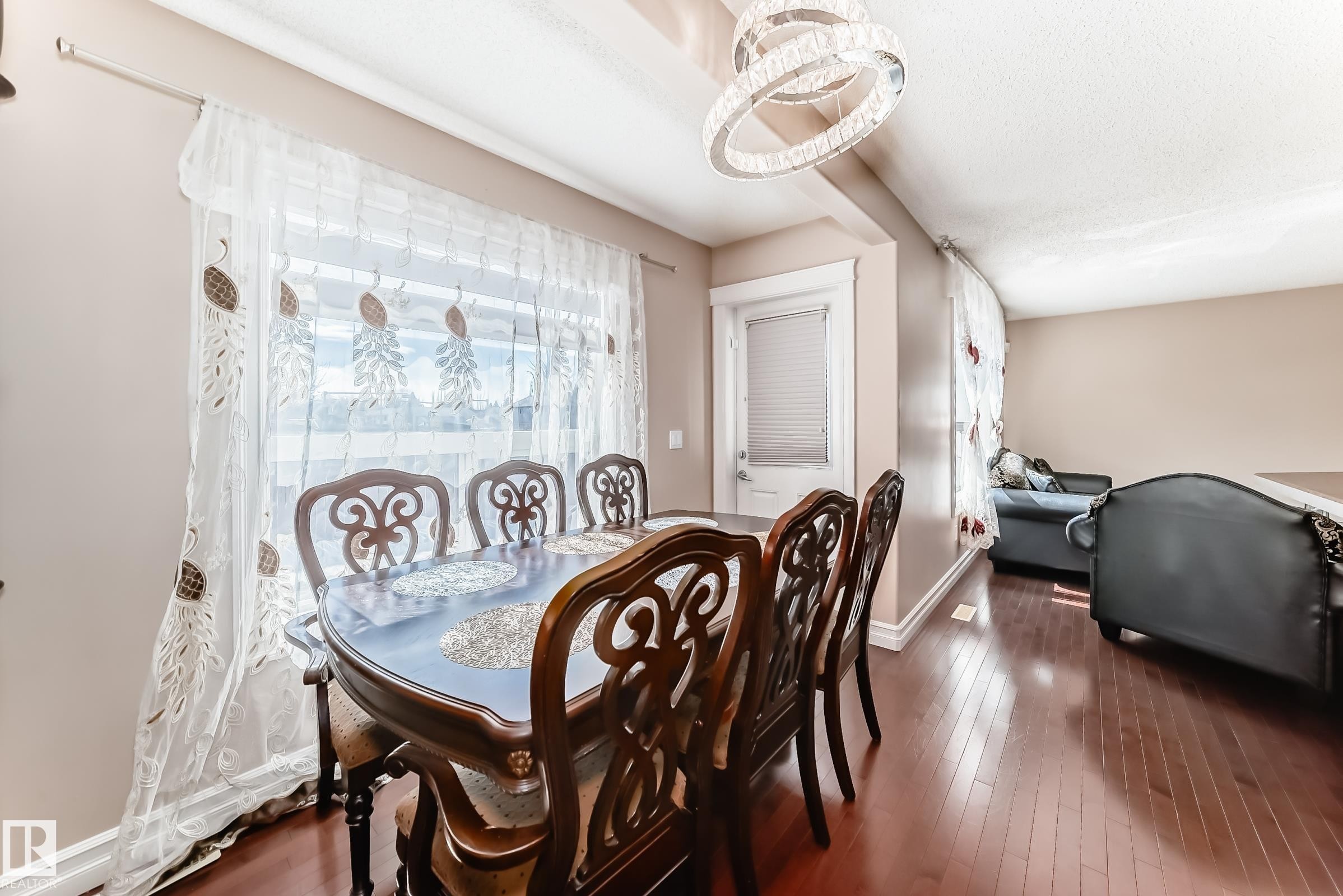 The dining area features a large window with sheer curtains, hardwood flooring, and a modern chandelier - 11415 167A Avenue Nw, Edmonton, AB - Indoor