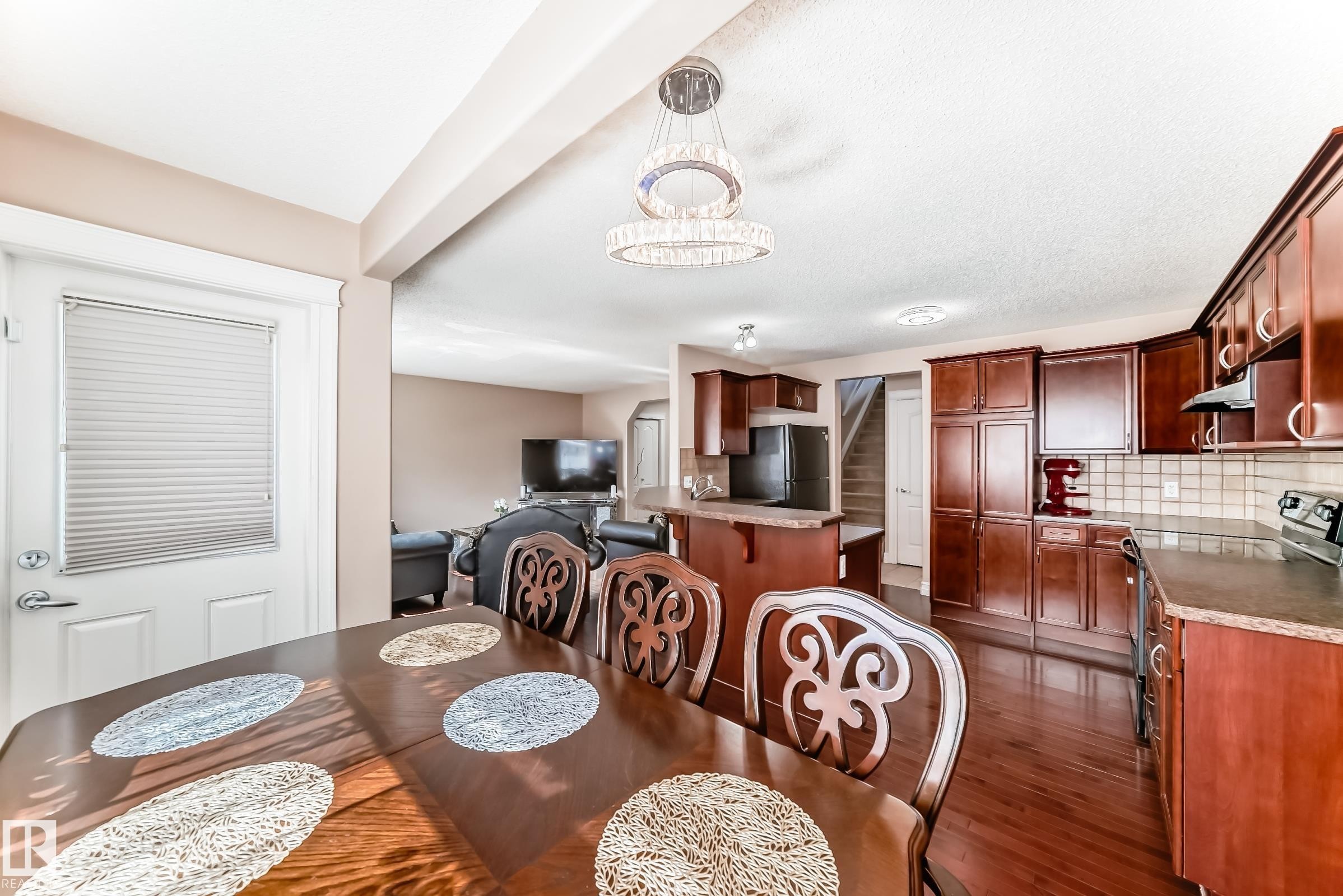 This open-concept main floor features rich hardwood flooring, a dining area with an elegant chandelier, and a kitchen equipped with dark wood cabinetry, a tile backsplash, and dark countertops - 11415 167A Avenue Nw, Edmonton, AB - Indoor