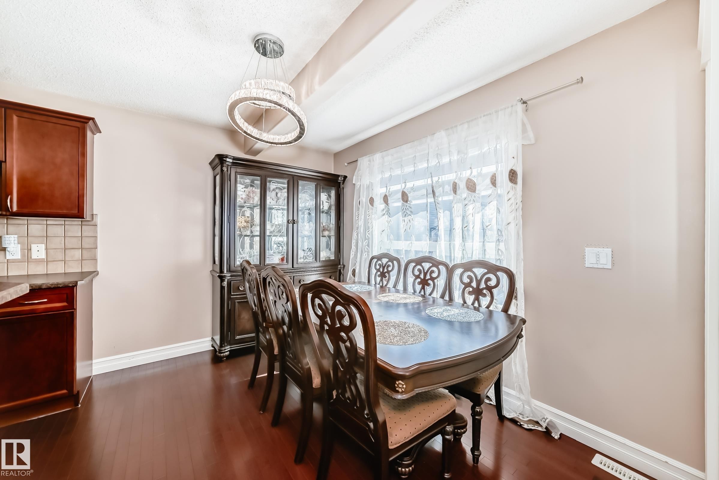 Dining area featuring hardwood floors, a large window with sheer curtains, and an elegant chandelier - 11415 167A Avenue Nw, Edmonton, AB - Indoor Photo Showing Dining Room