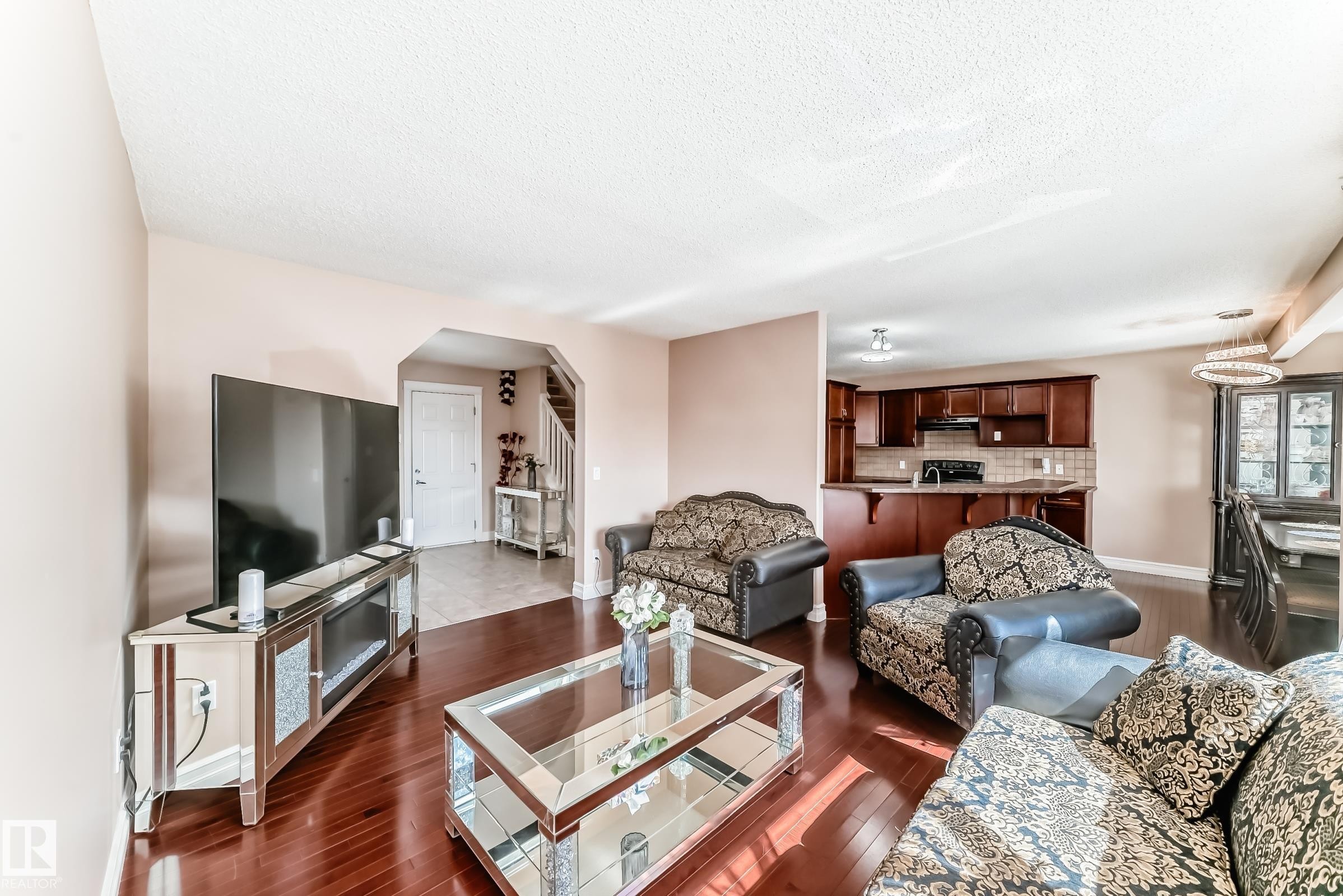 The open concept living area features hardwood flooring, a clear view of the kitchen with dark wood cabinetry and a breakfast bar, and a distinct dining area with a modern chandelier - 11415 167A Avenue Nw, Edmonton, AB - Indoor Photo Showing Living Room