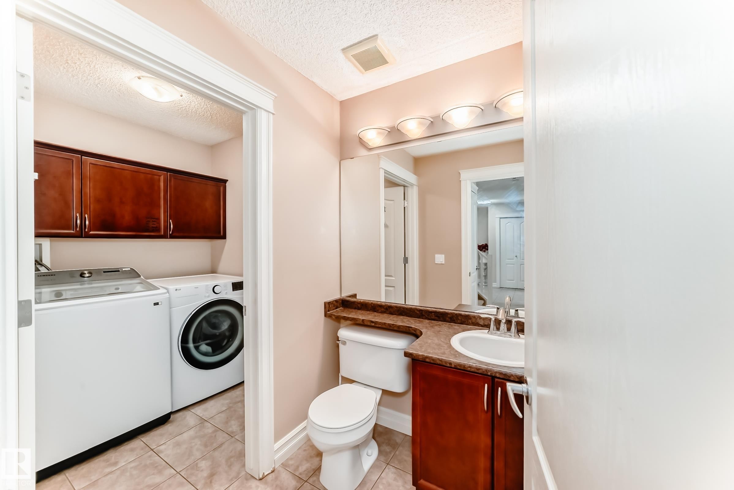 This property features a bathroom with a vanity, sink, and toilet, and an adjacent laundry area with a washer, dryer, and dark wood cabinetry - 11415 167A Avenue Nw, Edmonton, AB - Indoor Photo Showing Laundry Room