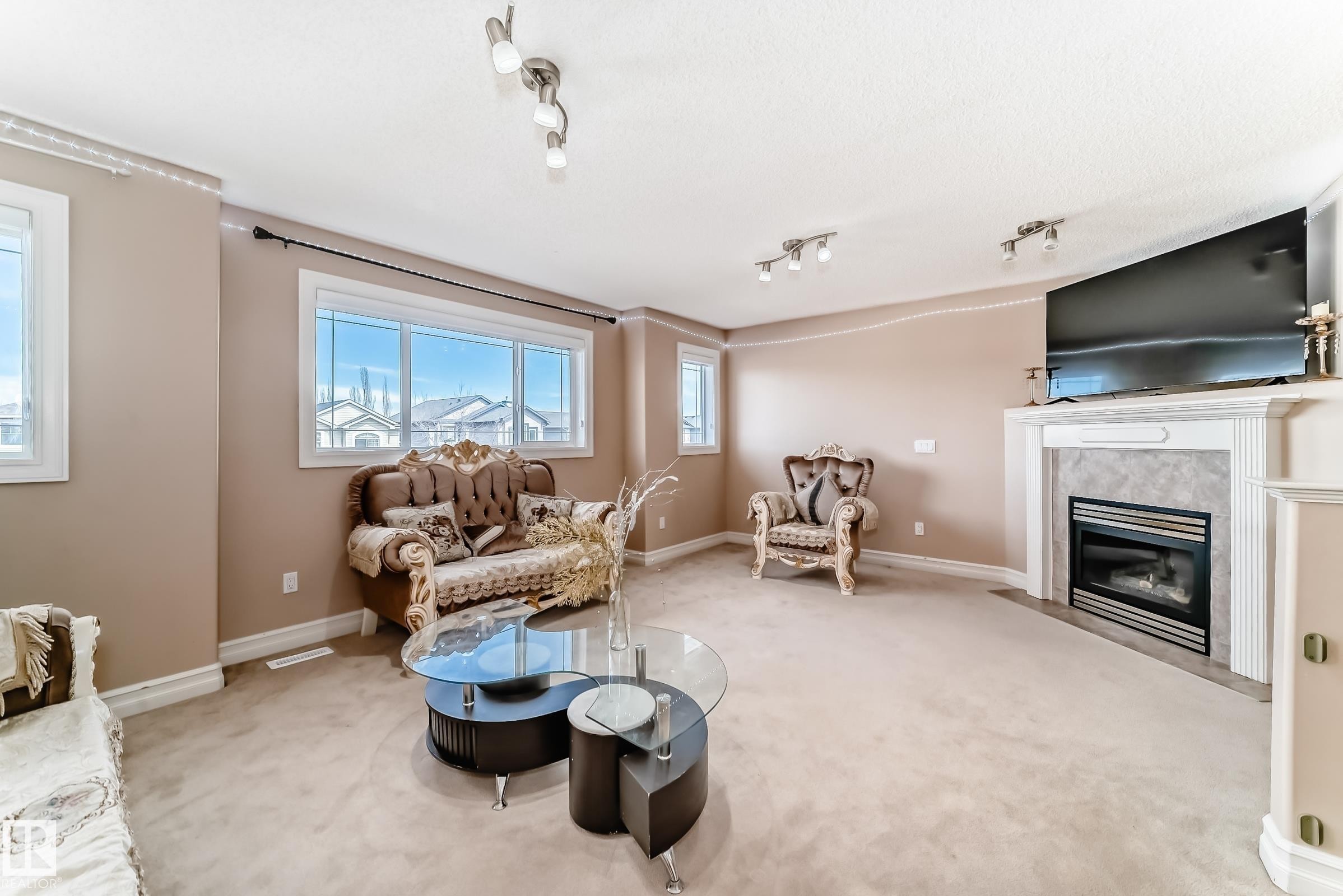 The living room features large windows, carpeted flooring, and a fireplace with a mantel - 11415 167A Avenue Nw, Edmonton, AB - Indoor Photo Showing Living Room With Fireplace