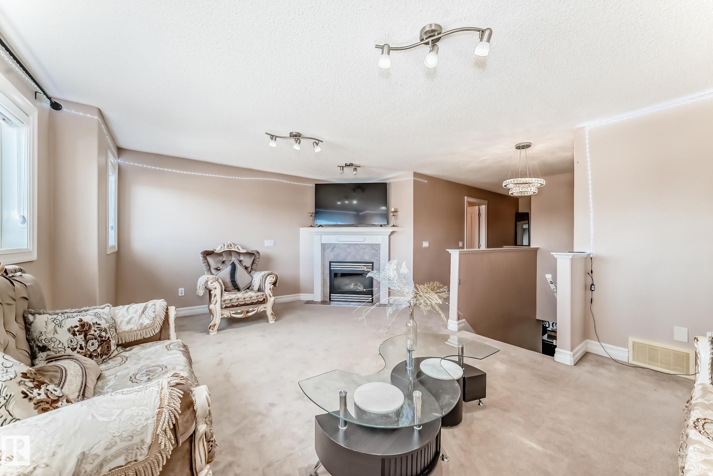Living area featuring carpet flooring, a fireplace with a stone surround, and windows providing natural light - 11415 167A Avenue Nw, Edmonton, AB - Indoor Photo Showing Living Room With Fireplace