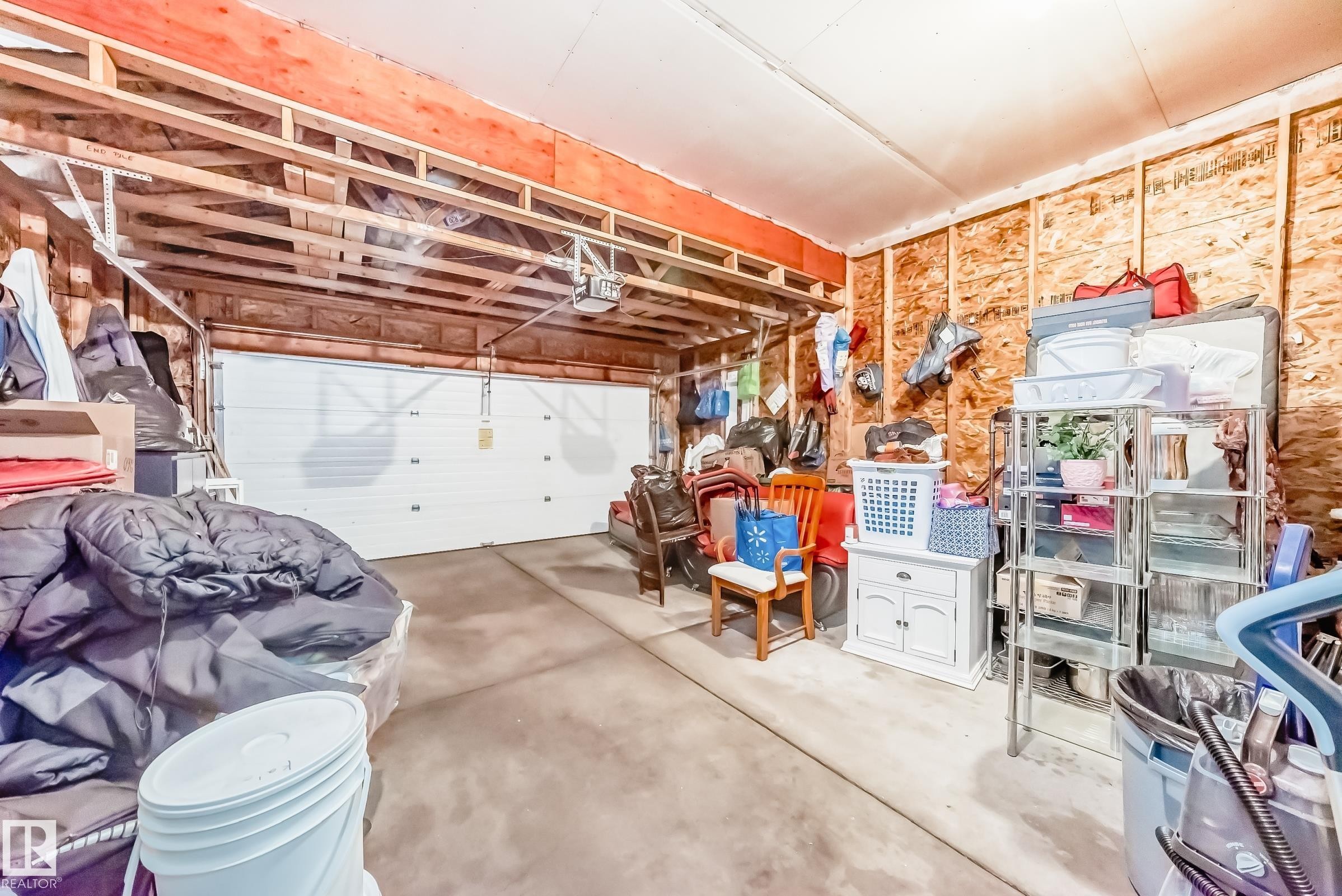 The property includes a spacious garage with a white overhead door, concrete flooring, and exposed wooden framing on the walls and ceiling - 11415 167A Avenue Nw, Edmonton, AB - Indoor Photo Showing Garage