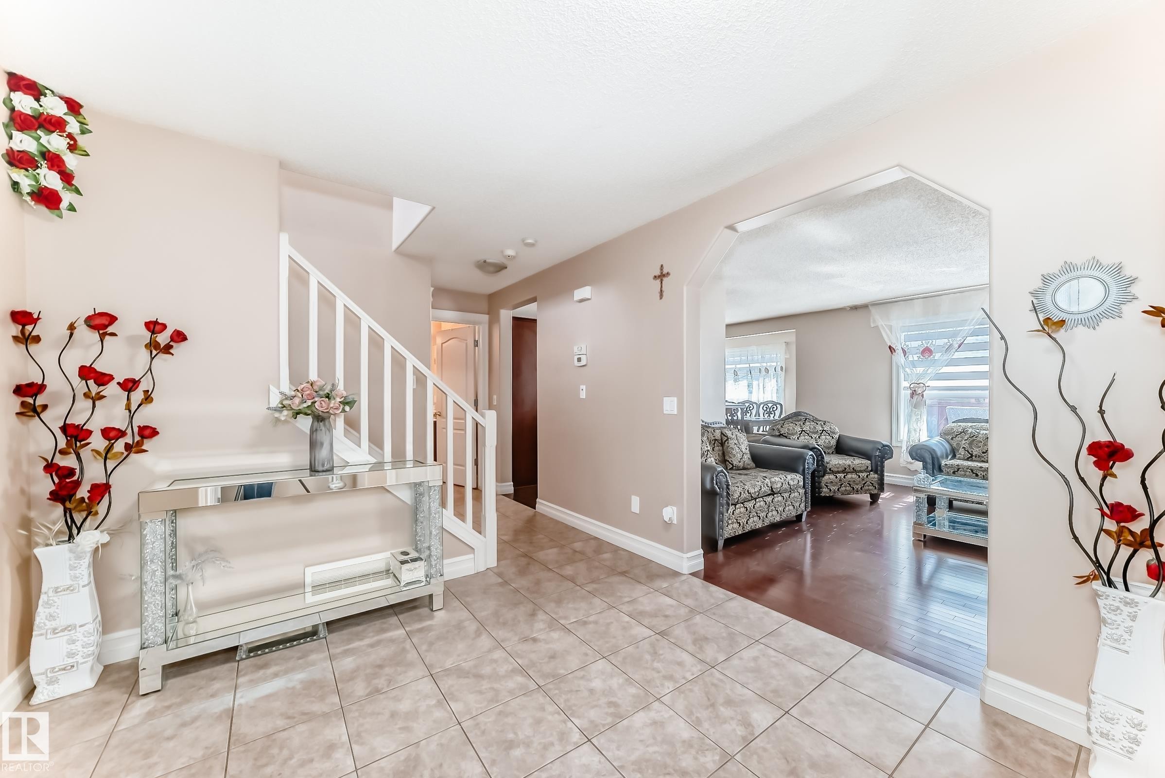The foyer features tiled flooring and a staircase with white railings, leading to an arched entryway revealing a living area with hardwood floors - 11415 167A Avenue Nw, Edmonton, AB - Indoor Photo Showing Other Room