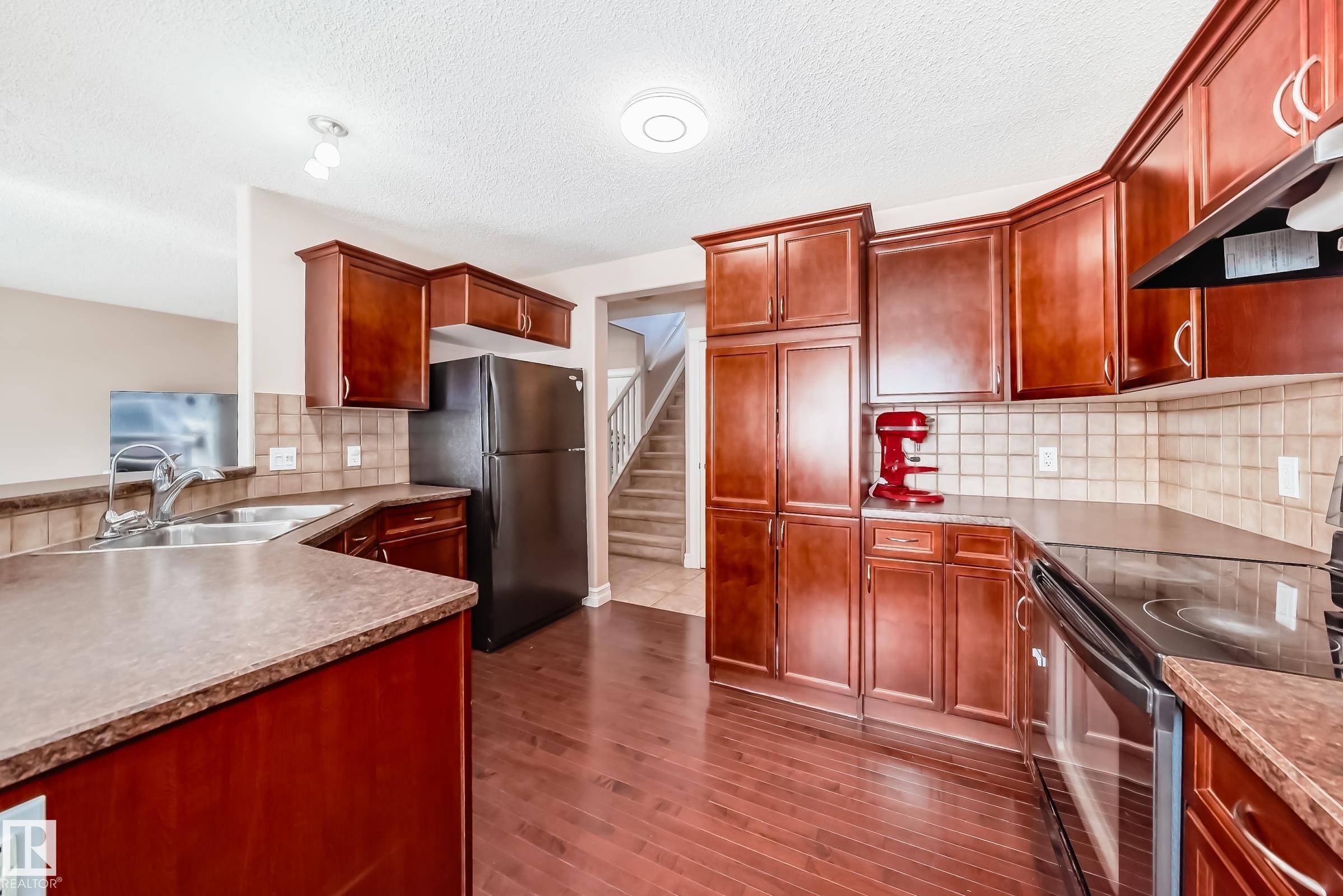 The kitchen features extensive dark wood cabinetry, a double basin stainless steel sink, and a black range with an overhead vent - 11415 167A Avenue Nw, Edmonton, AB - Indoor Photo Showing Kitchen With Double Sink