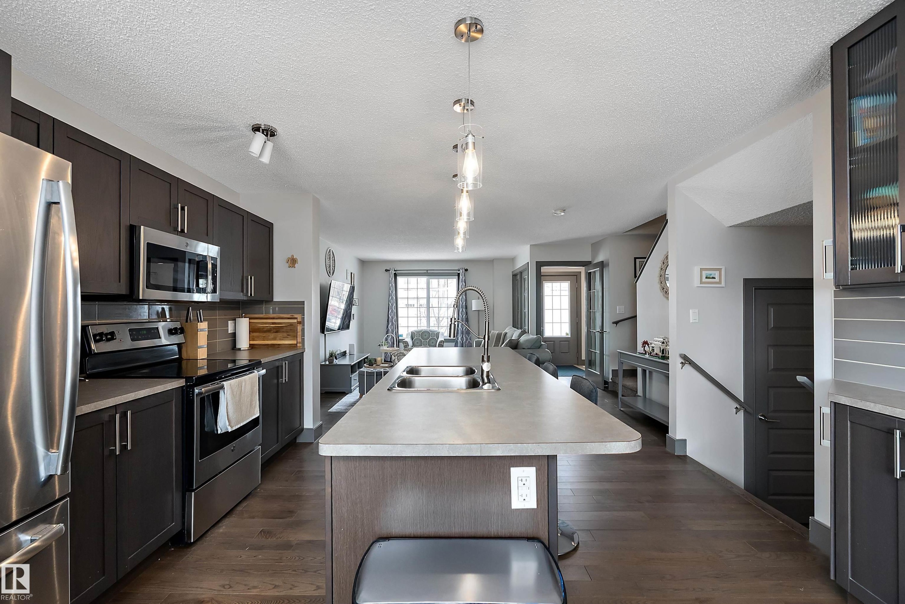 The kitchen features dark wood cabinetry, stainless steel appliances, and a central island with a double sink and pendant lighting - 7776 Eifert Crescent Nw, Edmonton, AB - Indoor Photo Showing Kitchen With Double Sink With Upgraded Kitchen