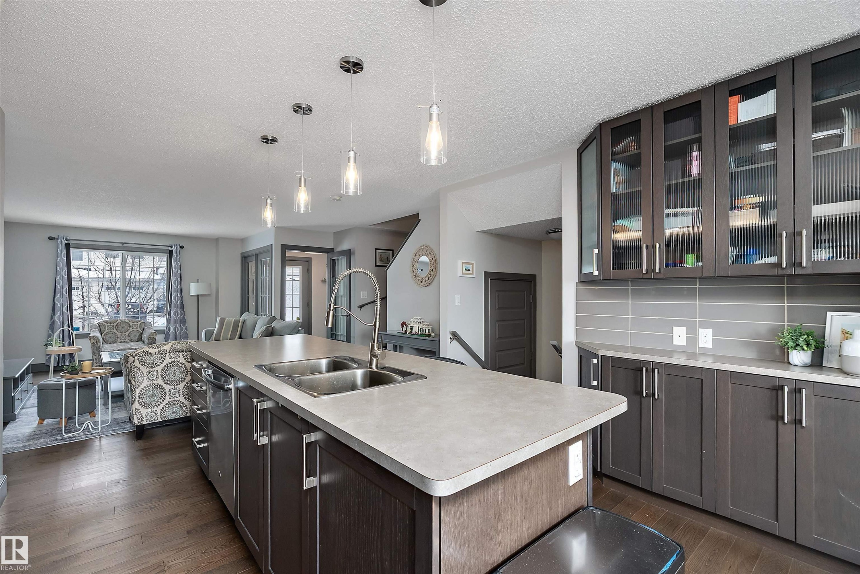 The kitchen features a large island with a double sink, pendant lighting, and dark wood cabinetry with glass fronts - 7776 Eifert Crescent Nw, Edmonton, AB - Indoor Photo Showing Kitchen With Double Sink With Upgraded Kitchen