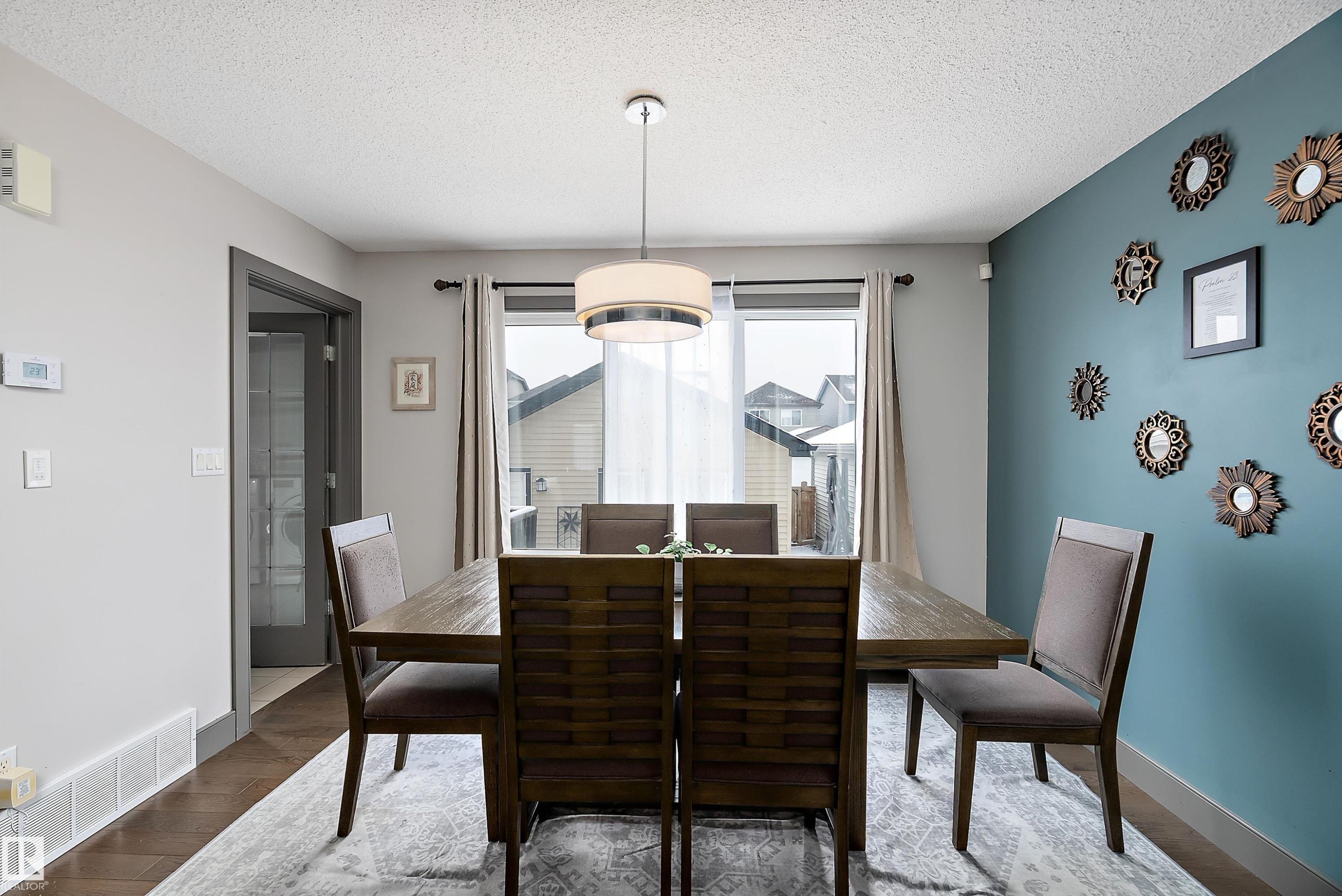 Dining area featuring a modern chandelier, hardwood flooring, and a large window providing natural light - 7776 Eifert Crescent Nw, Edmonton, AB - Indoor Photo Showing Dining Room