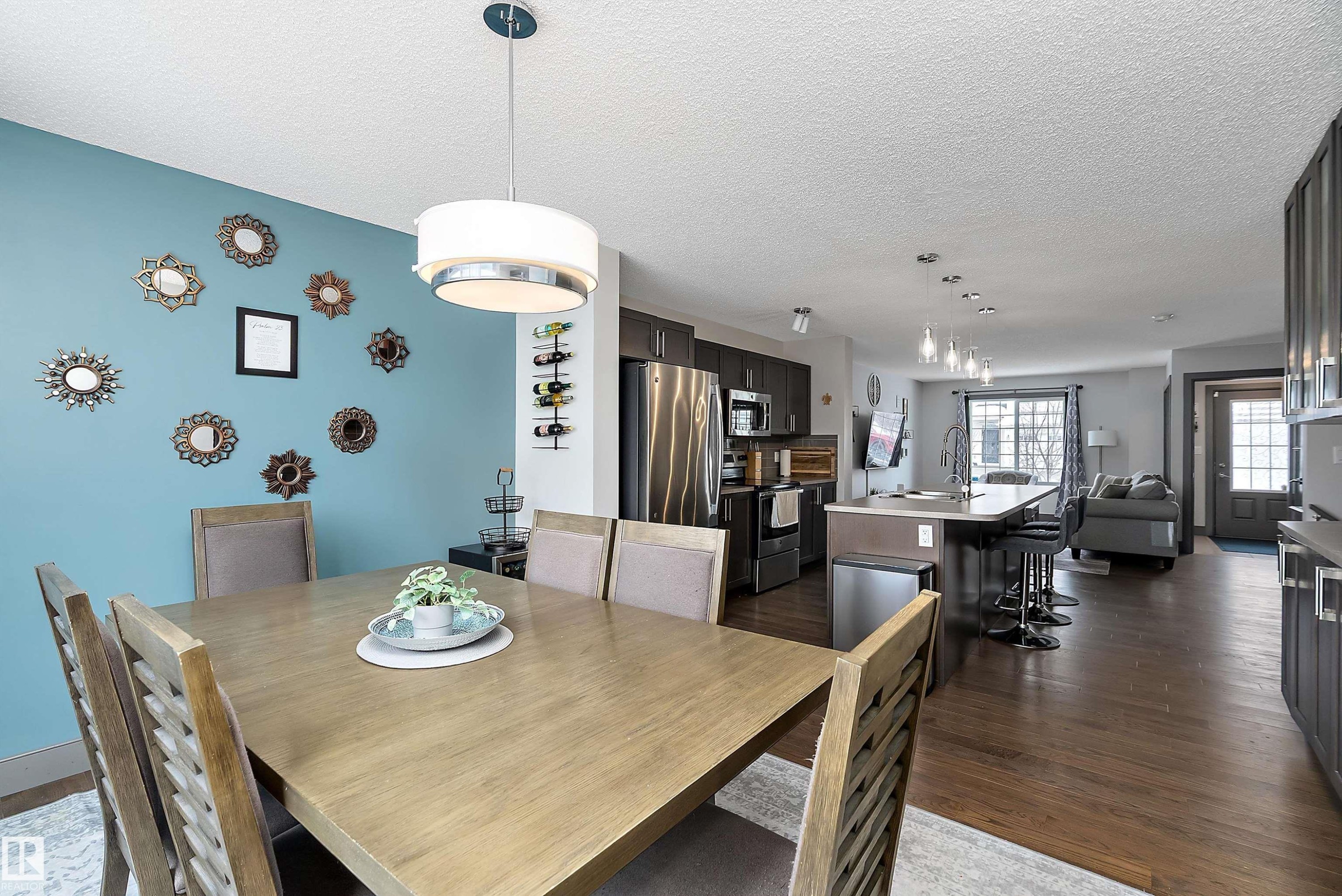 The property features an open-concept living space with dark wood flooring, a dining area with a modern chandelier, and a kitchen with stainless steel appliances and dark cabinetry - 7776 Eifert Crescent Nw, Edmonton, AB - Indoor Photo Showing Dining Room