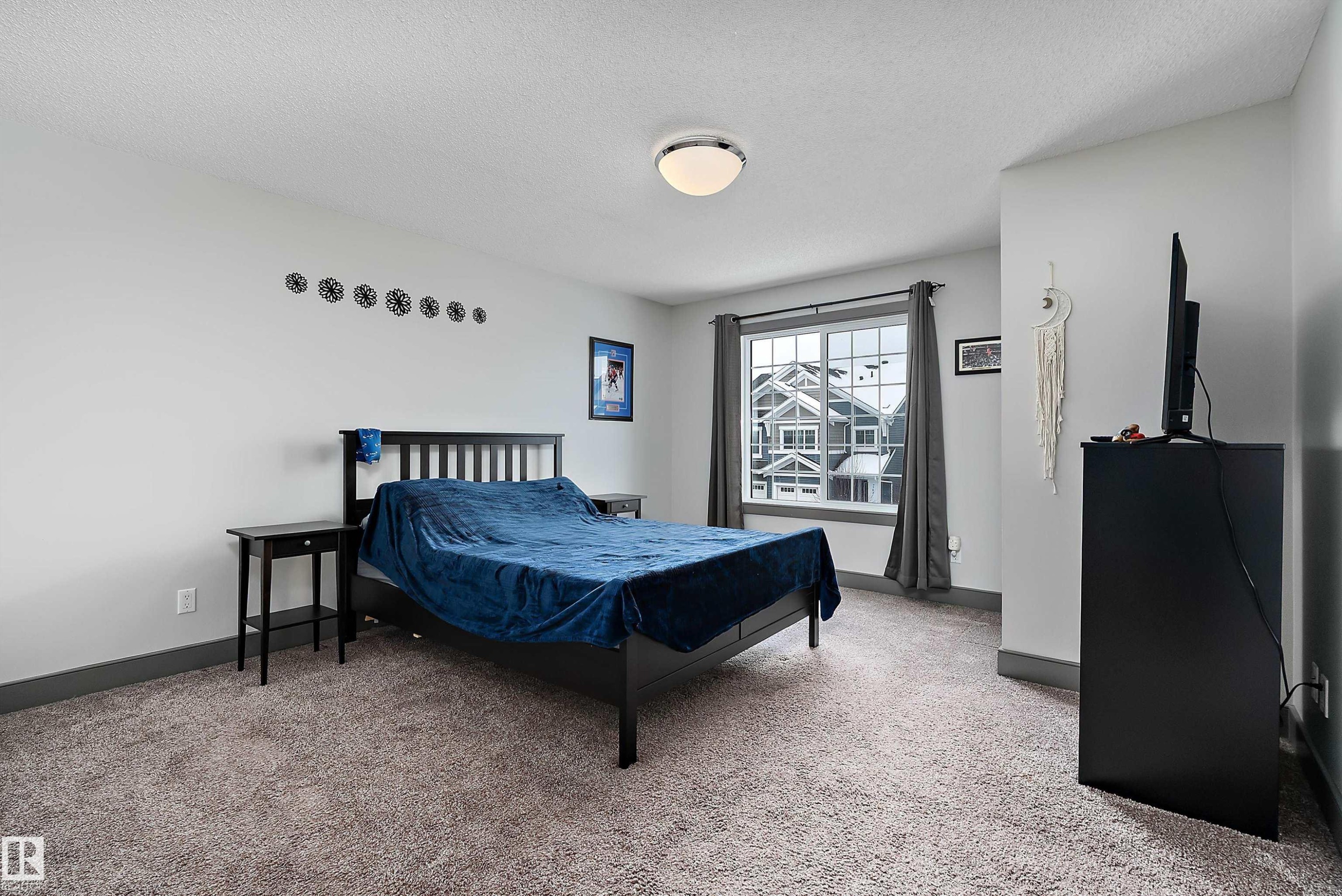 This room features light-colored walls, carpeted flooring, and a window with a view of the surrounding architecture - 7776 Eifert Crescent Nw, Edmonton, AB - Indoor Photo Showing Bedroom
