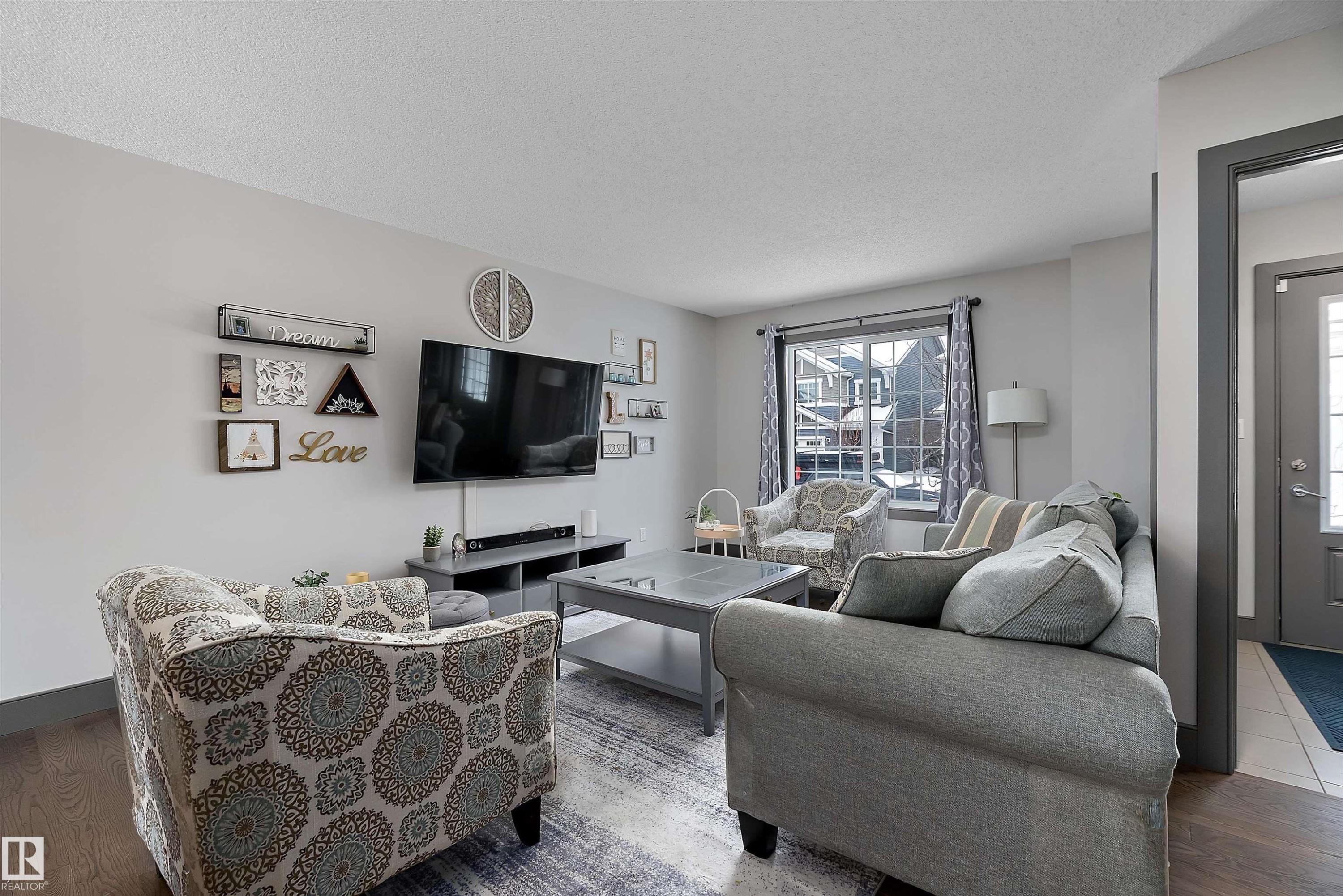 The living area features a large window with white casing, a ceiling with a textured finish, and light-colored walls - 7776 Eifert Crescent Nw, Edmonton, AB - Indoor Photo Showing Living Room