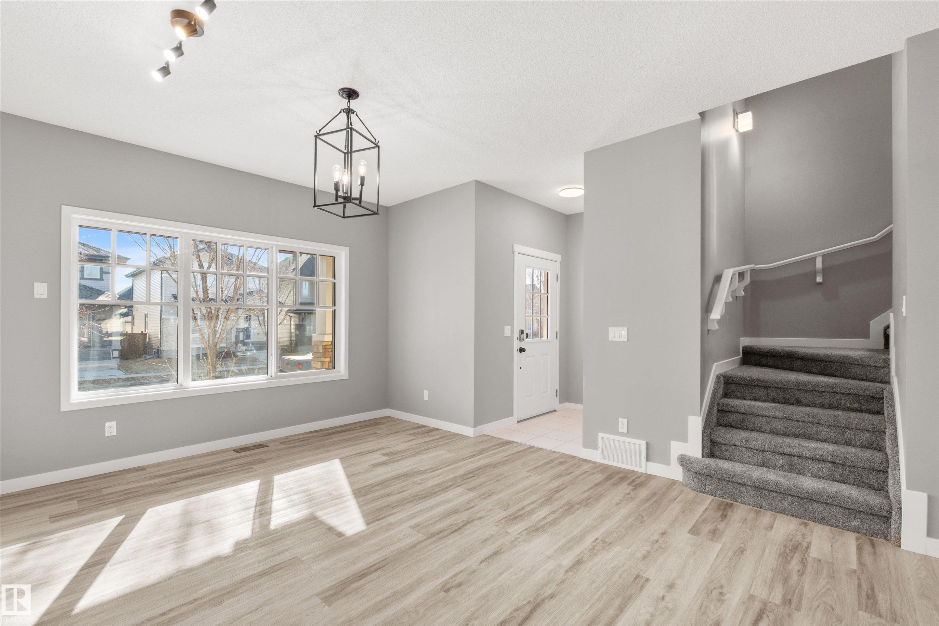 Inviting interior space featuring light-colored flooring, a prominent window, and a carpeted staircase with a handrail - 4016 Allan Crescent, Edmonton, AB - Indoor Photo Showing Other Room