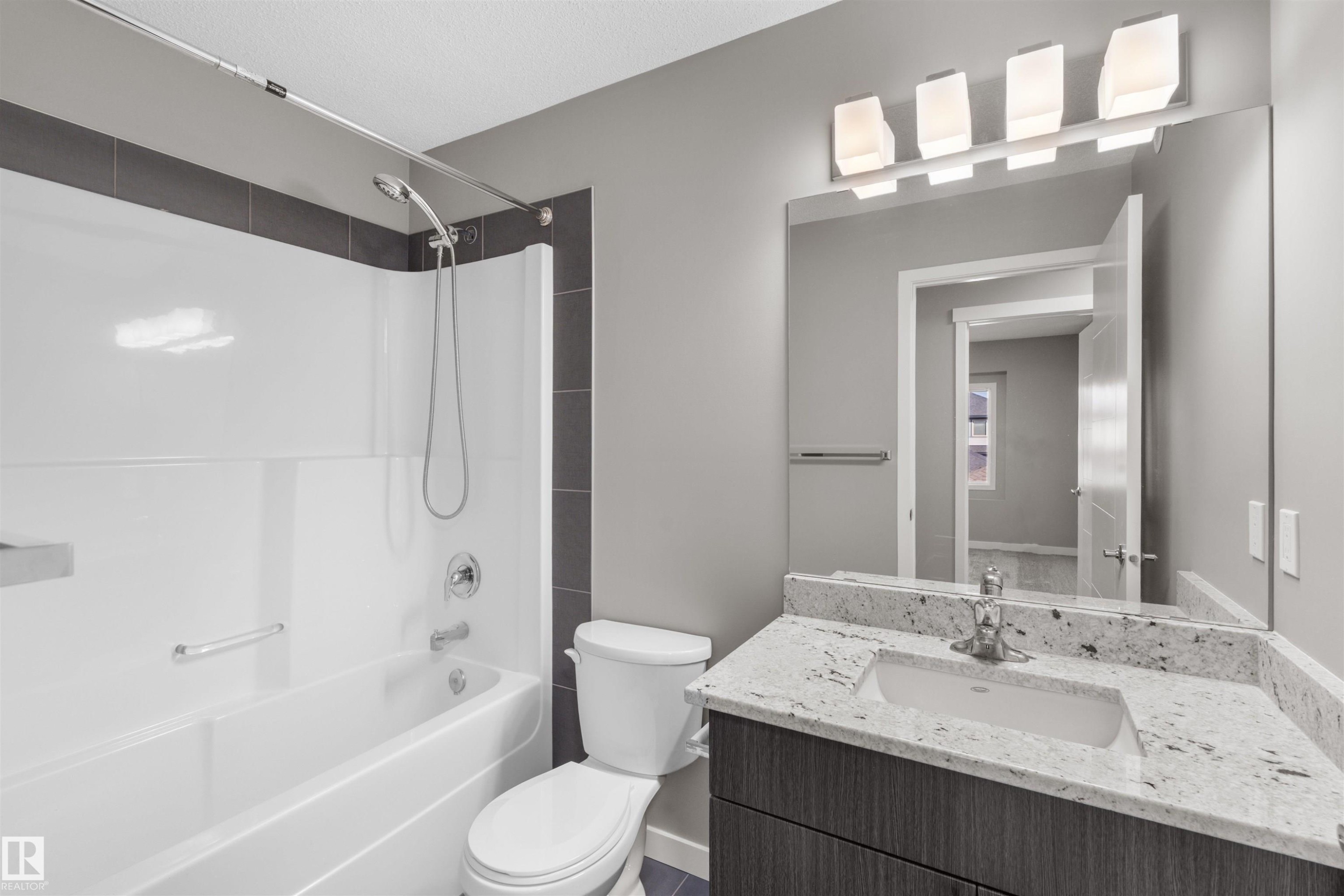 The bathroom features a white bathtub with a shower, a modern vanity with a granite countertop, and a large mirror - 4016 Allan Crescent, Edmonton, AB - Indoor Photo Showing Bathroom