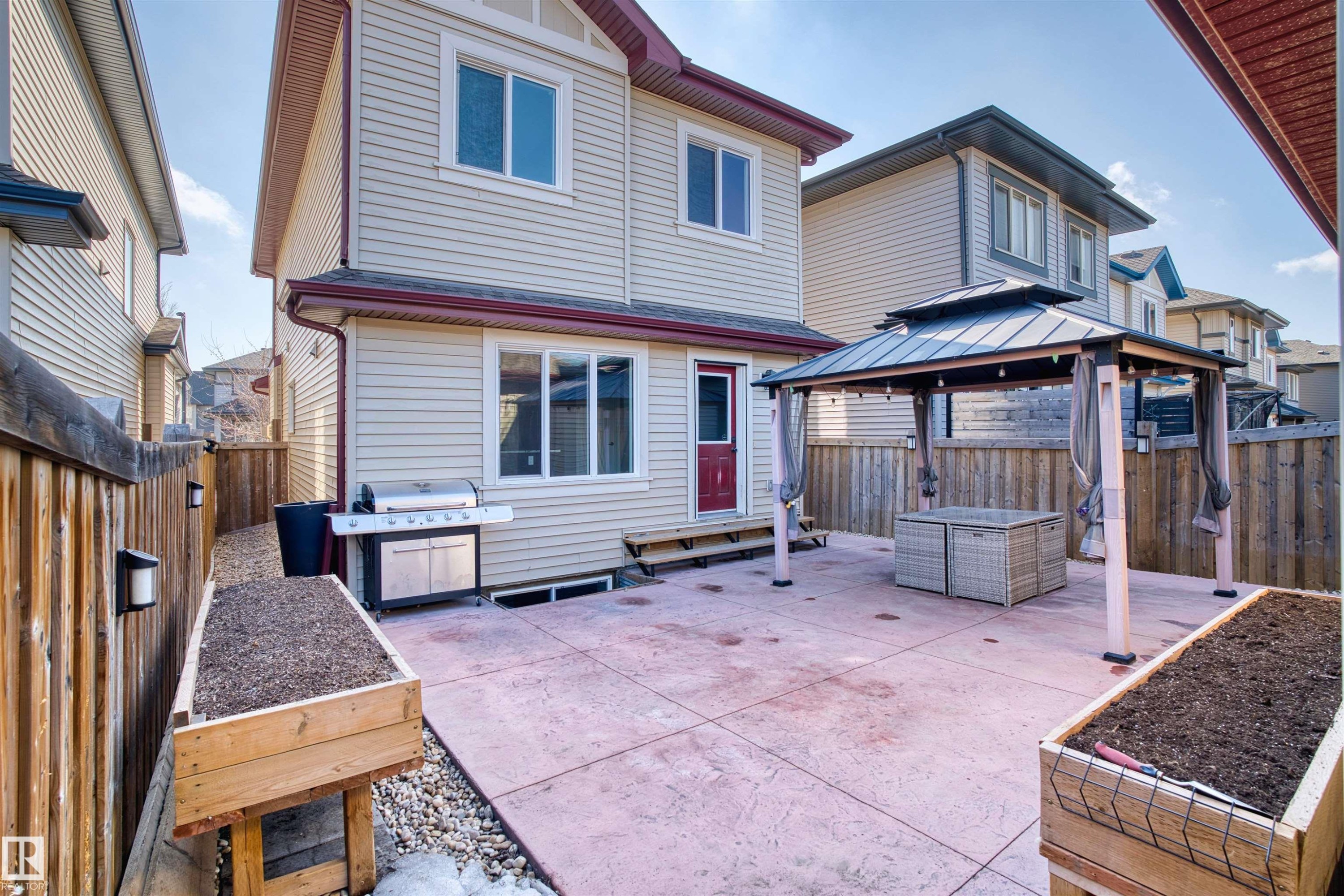 The property features a backyard with a large concrete patio, a gazebo with privacy curtains, and raised wooden garden beds - 4016 Allan Crescent, Edmonton, AB - Outdoor With Deck Patio Veranda With Exterior