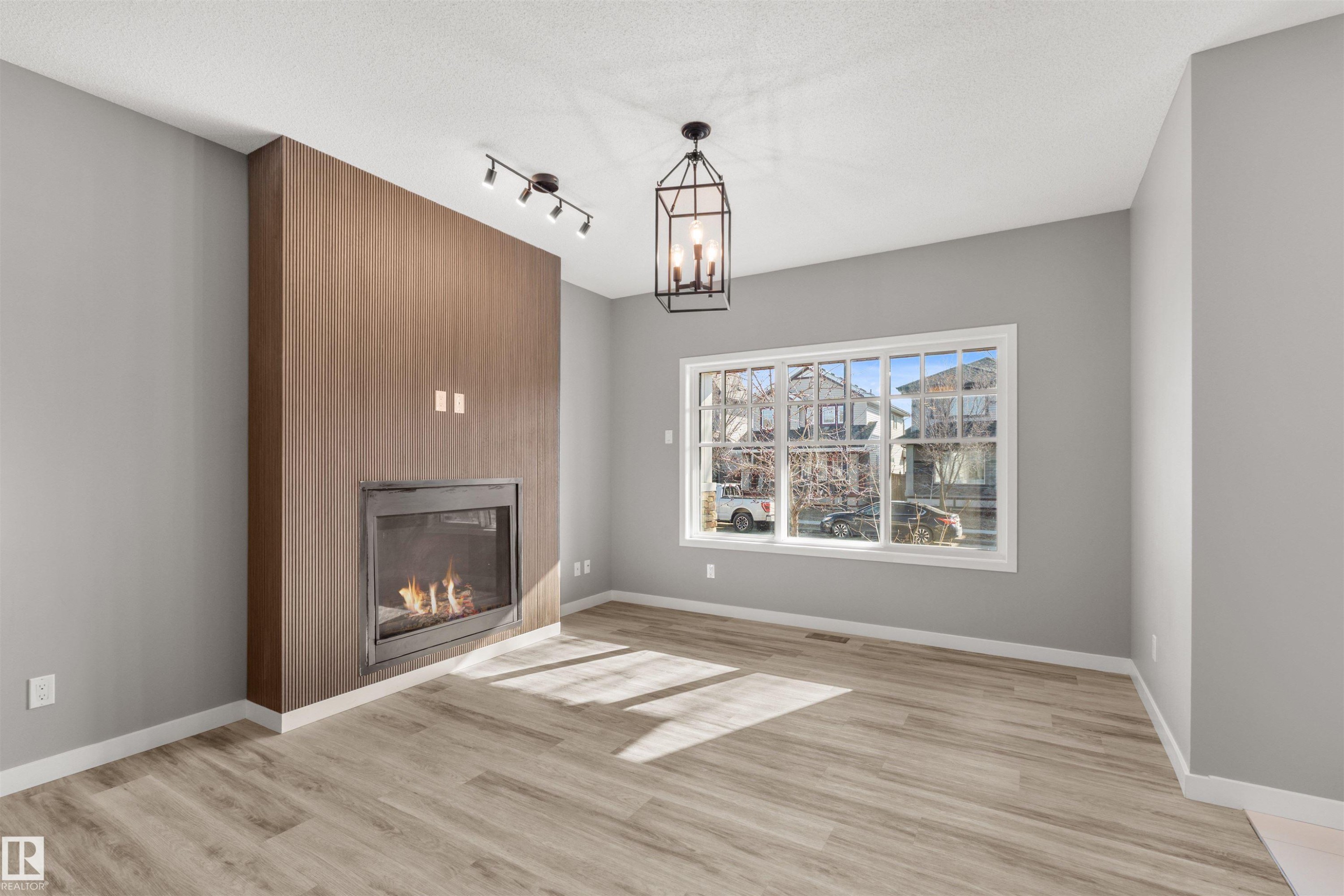 Living area featuring light gray walls, light-colored flooring, a fireplace with a wood-paneled surround, and a window with white trim - 4016 Allan Crescent, Edmonton, AB - Indoor Photo Showing Living Room With Fireplace