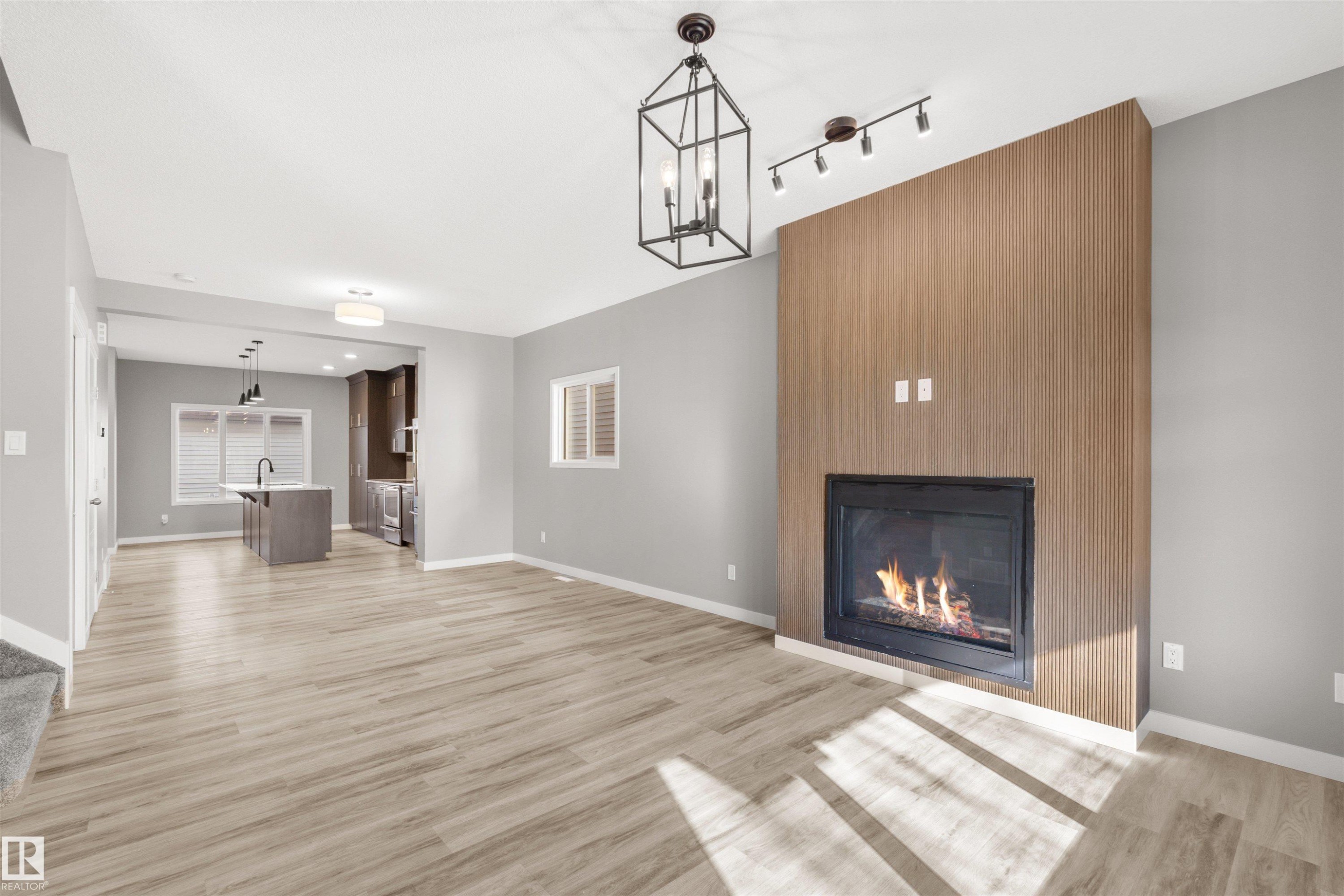 Living area featuring light wood-look flooring, a fireplace with a light wood-paneled surround, and an open layout leading to the kitchen - 4016 Allan Crescent, Edmonton, AB - Indoor Photo Showing Living Room With Fireplace
