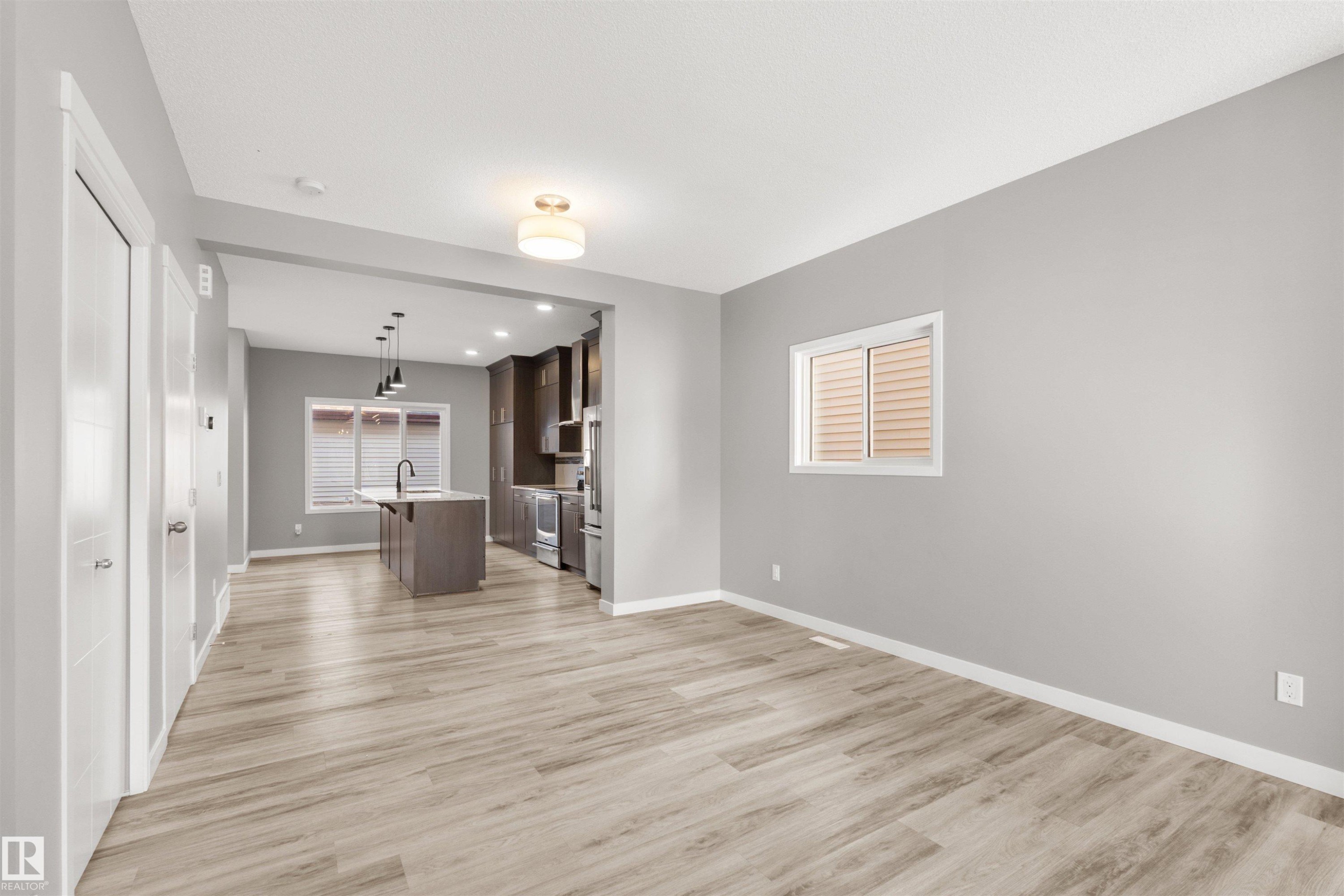 Open concept living area featuring light-toned flooring, neutral gray walls, and a window with horizontal blinds - 4016 Allan Crescent, Edmonton, AB - Indoor Photo Showing Other Room