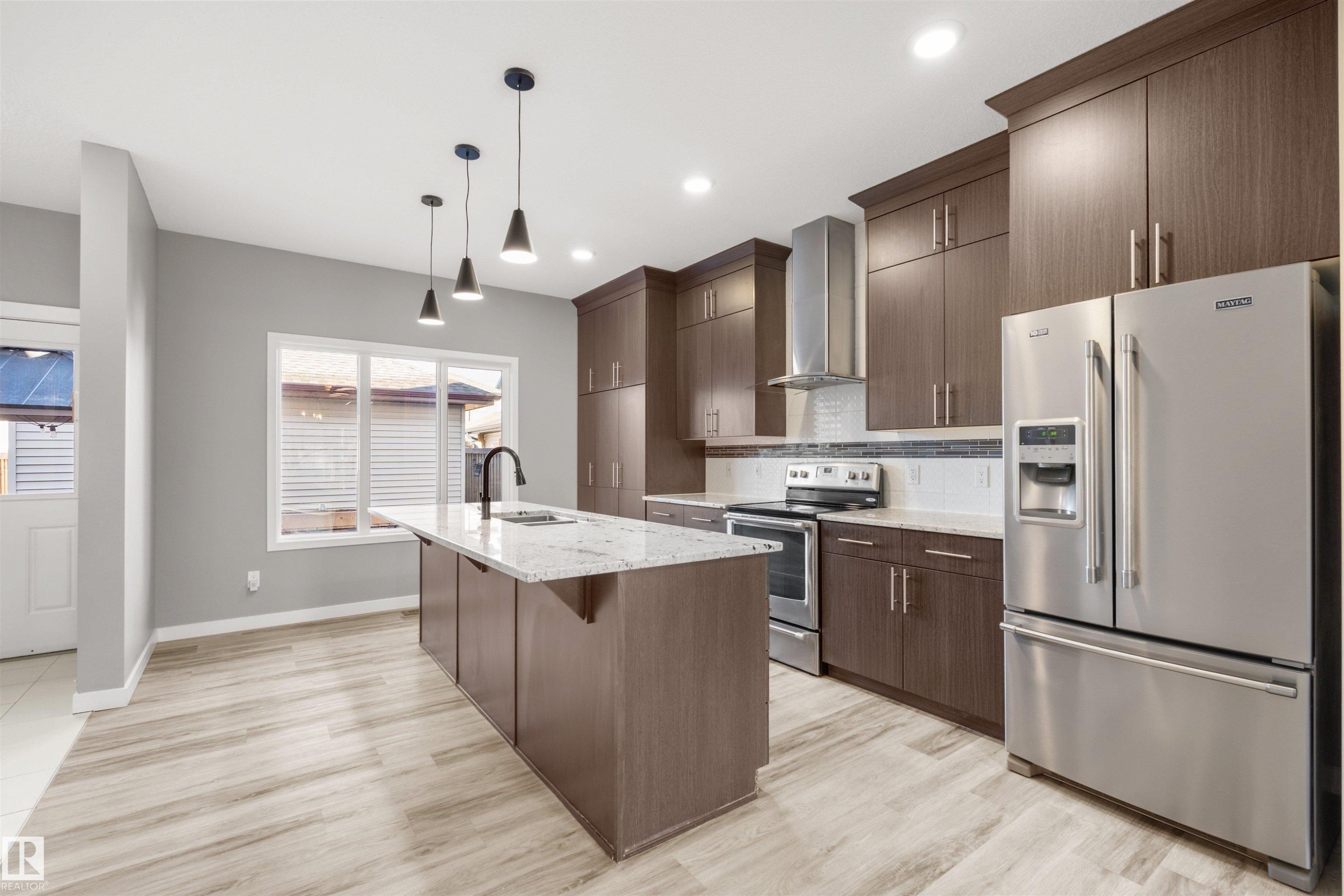 The kitchen features an island with a light-colored countertop, dark cabinetry, and stainless steel appliances - 4016 Allan Crescent, Edmonton, AB - Indoor Photo Showing Kitchen With Stainless Steel Kitchen With Upgraded Kitchen