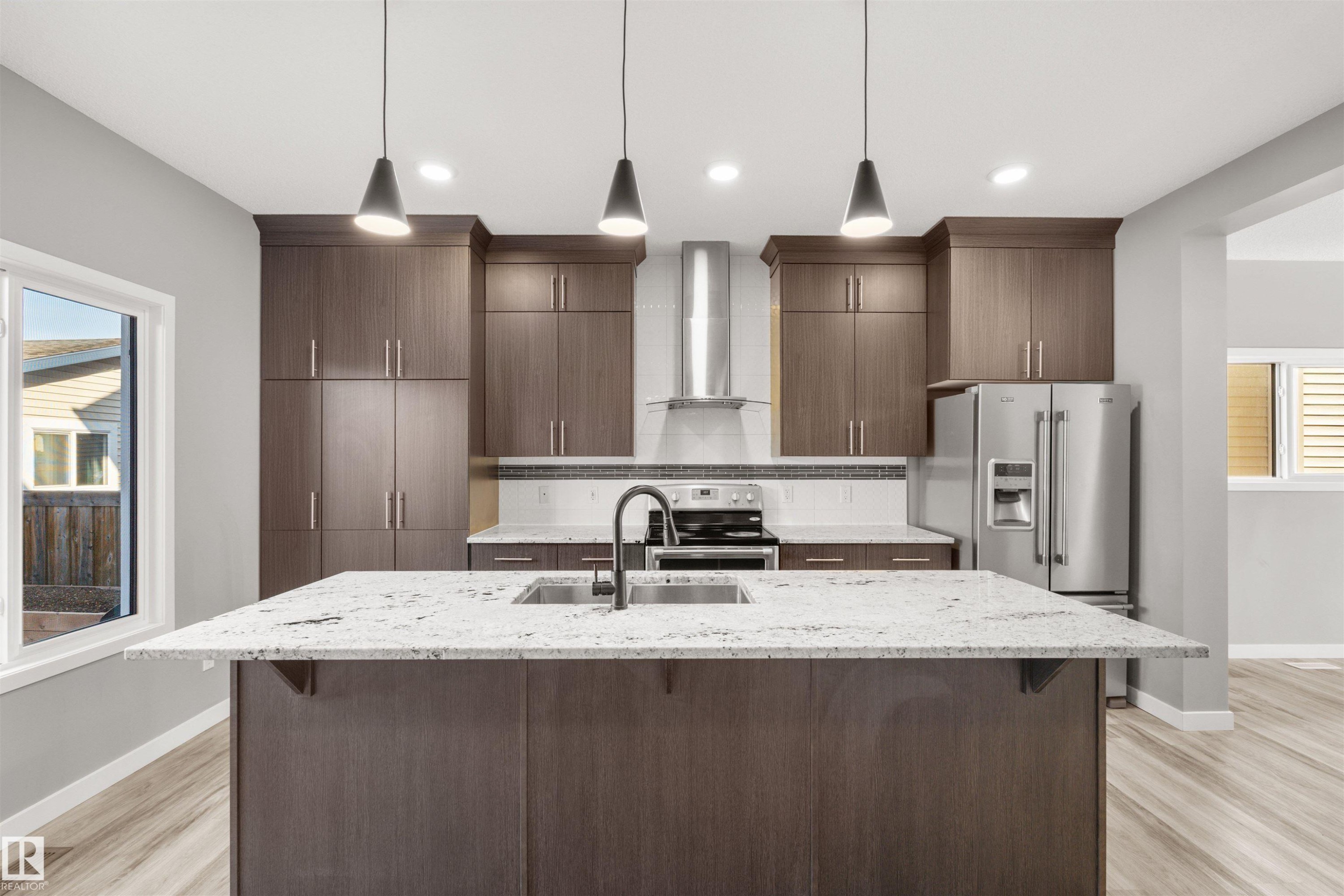 The kitchen features an island with a sink and a black faucet, granite countertops, dark wood cabinetry, and stainless steel appliances - 4016 Allan Crescent, Edmonton, AB - Indoor Photo Showing Kitchen With Upgraded Kitchen