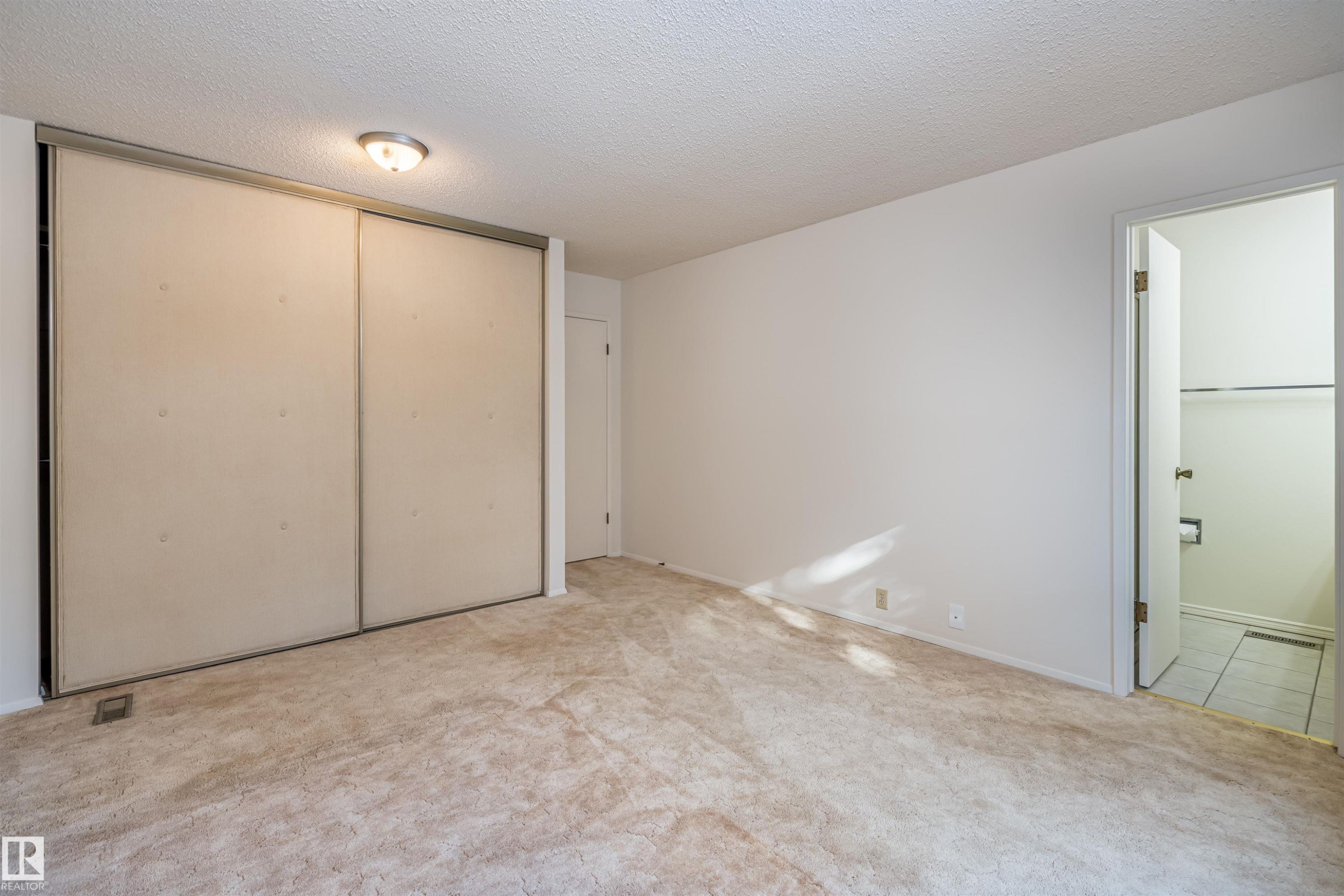 This room features light-colored carpeting, a wall-mounted light fixture, and a spacious closet with sliding doors - 108 Forest Grove, St. Albert, AB - Indoor Photo Showing Other Room