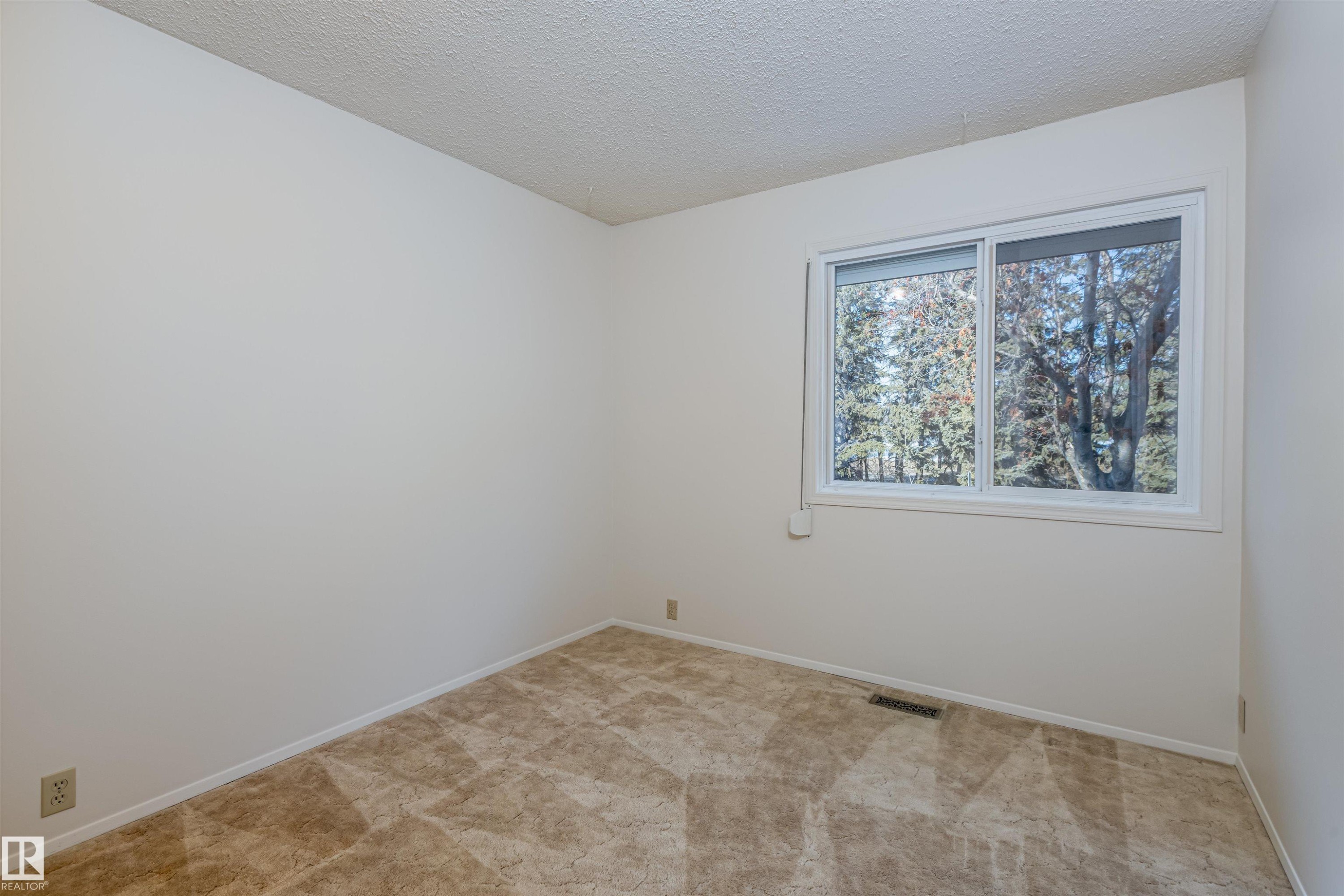 This room features light-colored walls, patterned carpeting, and a window offering views of mature trees - 108 Forest Grove, St. Albert, AB - Indoor Photo Showing Other Room