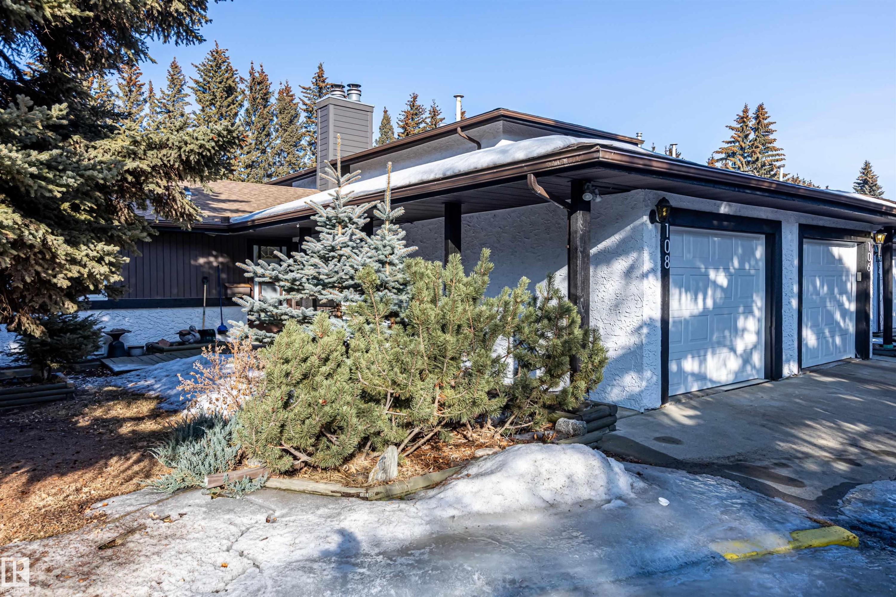 The property features a brown roof, white garage doors, and a combination of white stucco and dark wood paneling on its exterior - 108 Forest Grove, St. Albert, AB - Outdoor