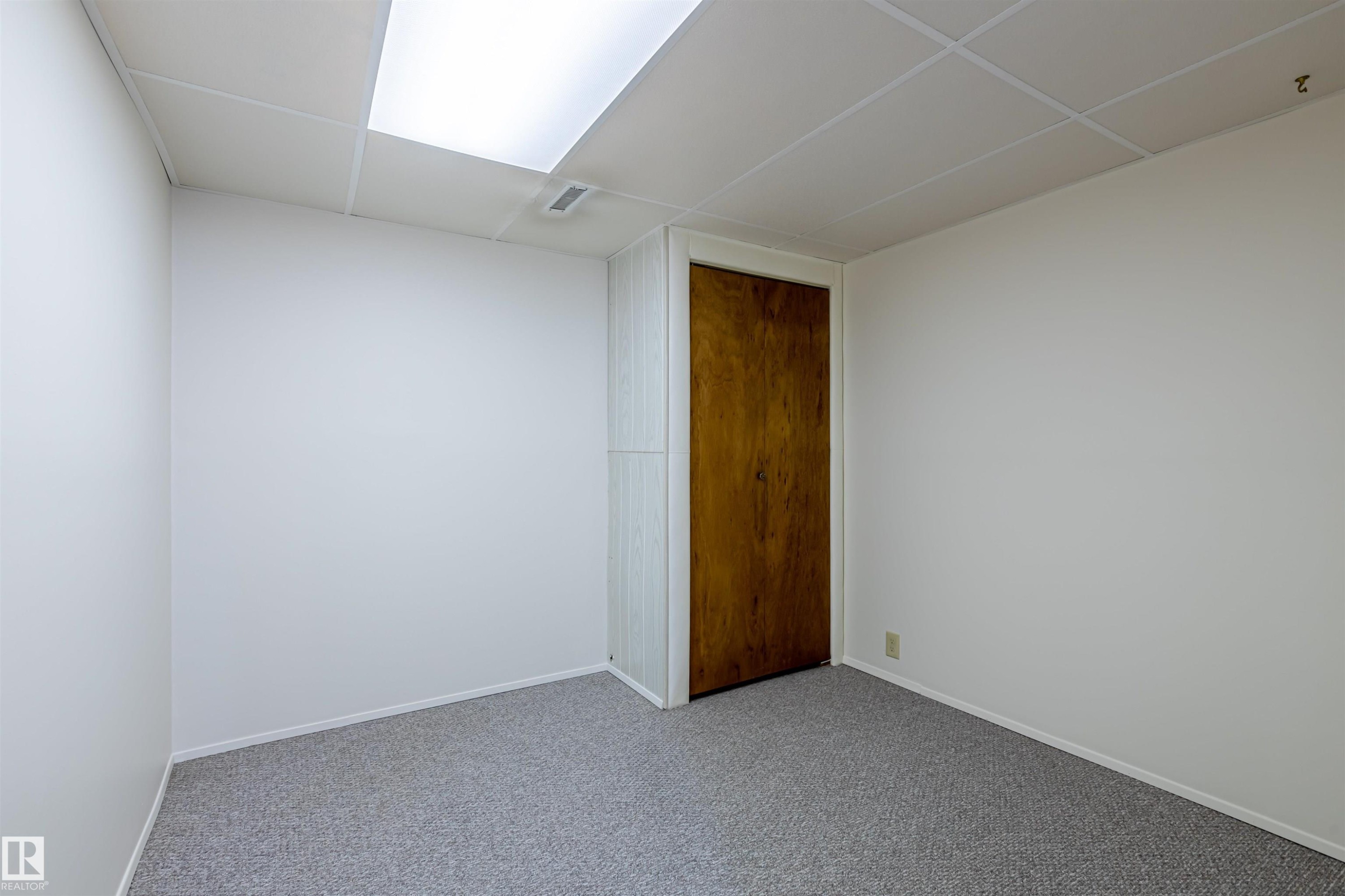 Room featuring light-colored walls, gray carpet, a wooden door, and a drop ceiling with integrated lighting - 108 Forest Grove, St. Albert, AB - Indoor Photo Showing Other Room