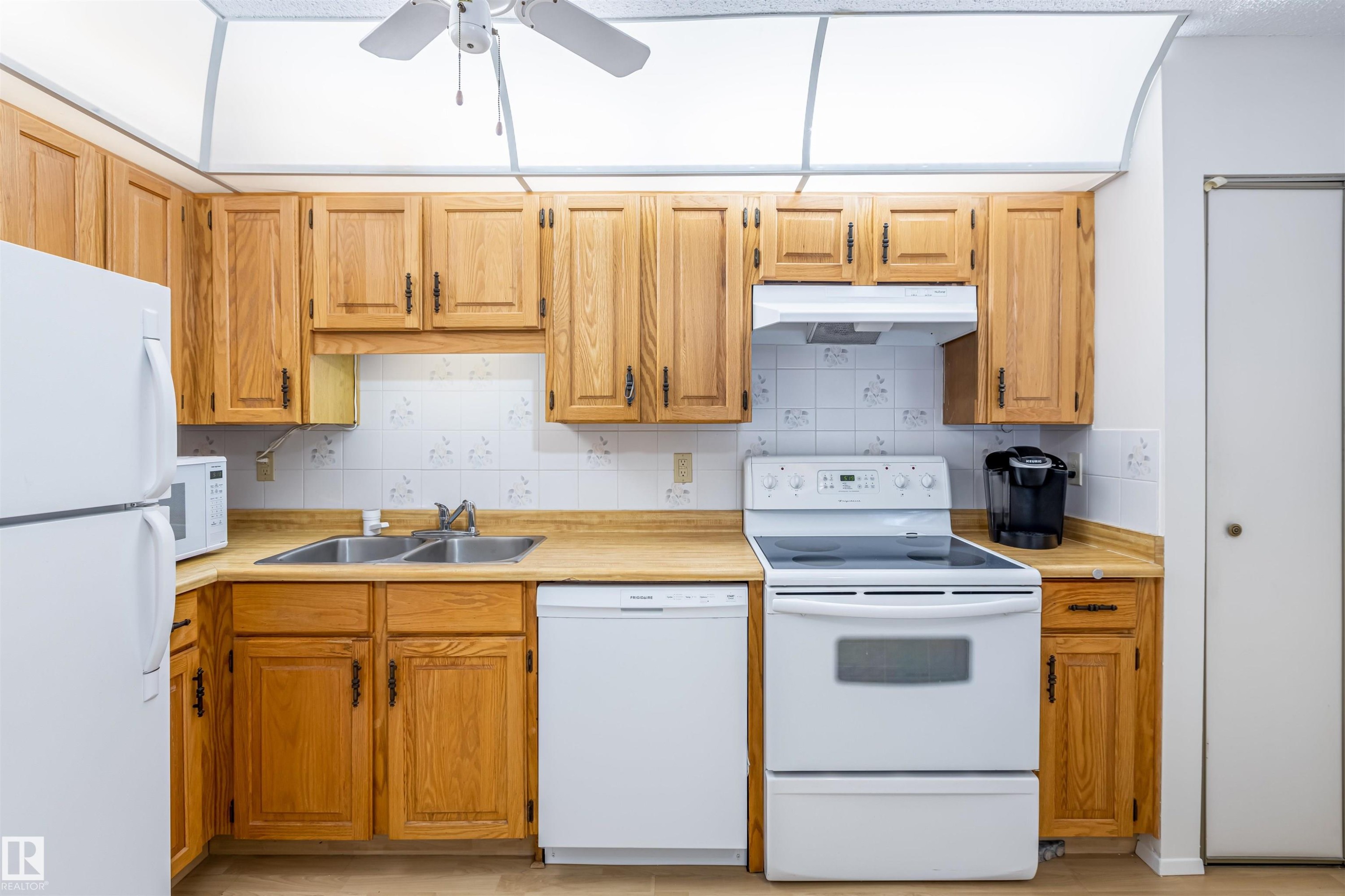 The property features a kitchen with wood cabinetry, a double basin stainless steel sink, and white appliances including a refrigerator, dishwasher, and range - 108 Forest Grove, St. Albert, AB - Indoor Photo Showing Kitchen With Double Sink