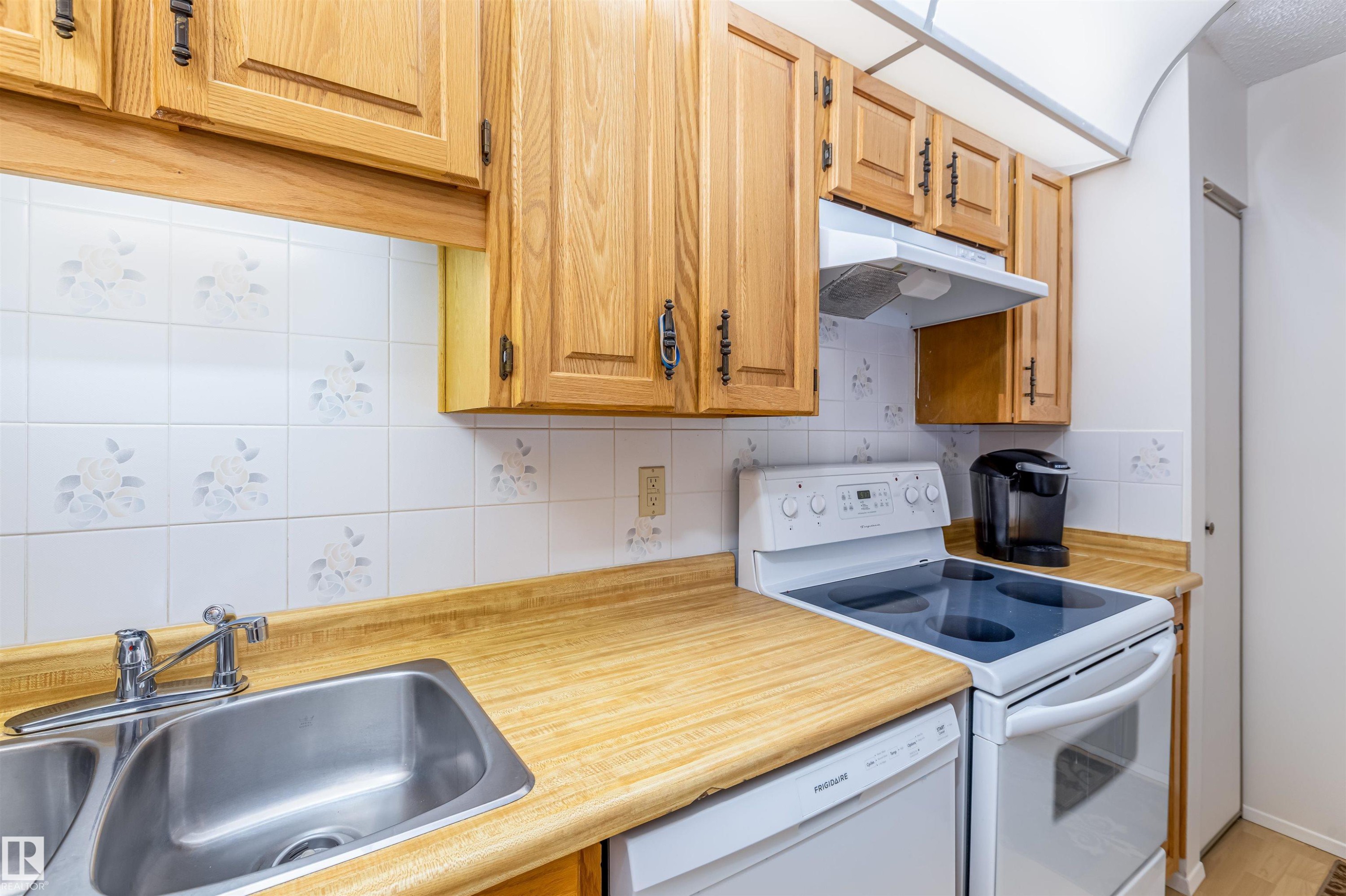 The kitchen features wood cabinetry, a double basin stainless steel sink, a white electric range, and a white dishwasher - 108 Forest Grove, St. Albert, AB - Indoor Photo Showing Kitchen With Double Sink