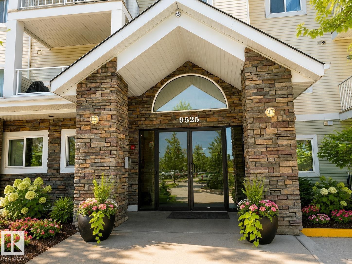 Building entrance with stone facade detailing, glass double doors, a prominent arched transom, and integrated address numbering - 336 9525 162 Avenue, Edmonton, AB - Outdoor With Balcony