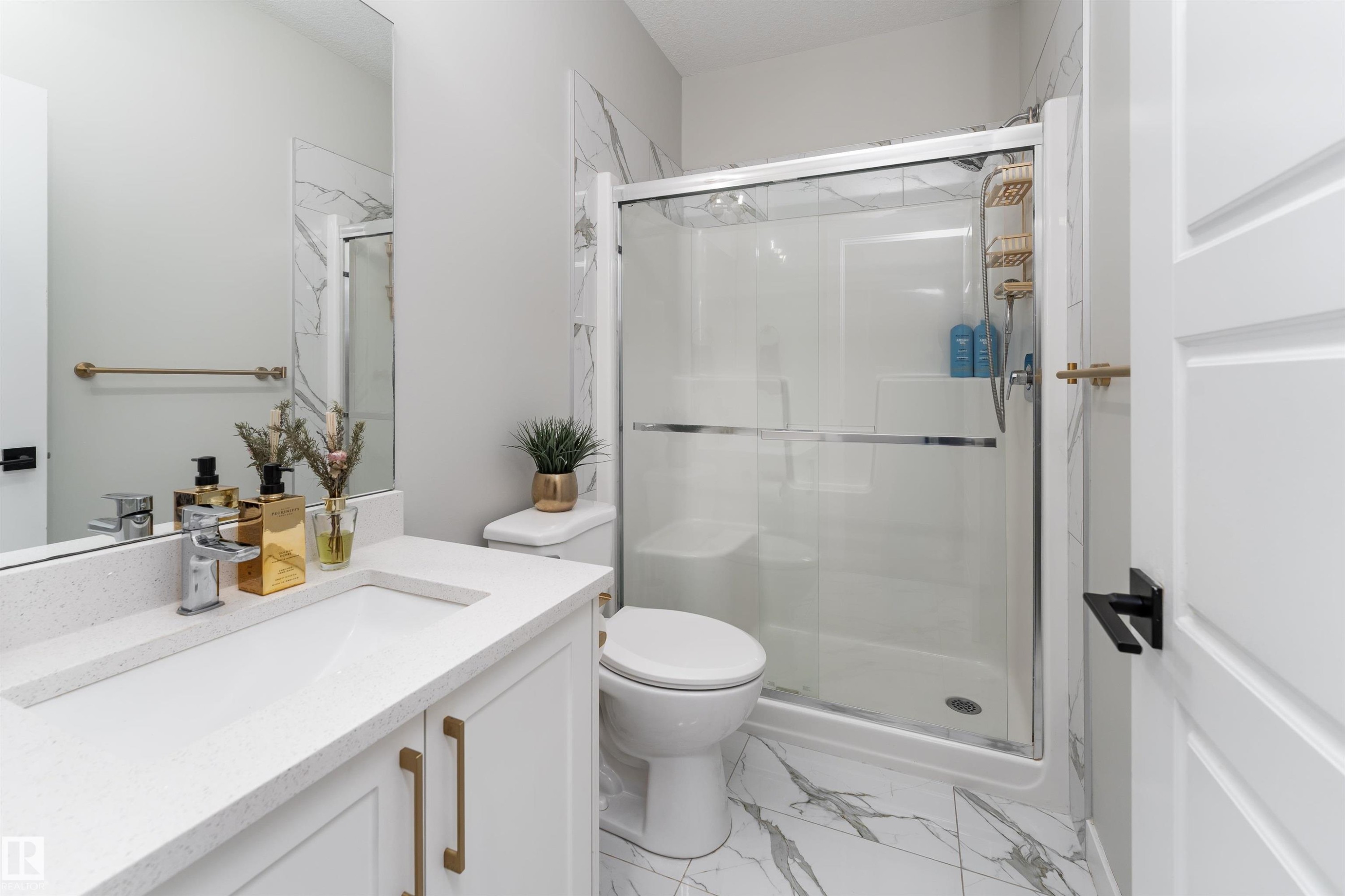 The bathroom features a modern vanity with a white countertop and gold-toned hardware, a spacious shower with a clear glass enclosure, and white marble-patterned floor tiles - 993 Berg Pl, Leduc, AB - Indoor Photo Showing Bathroom
