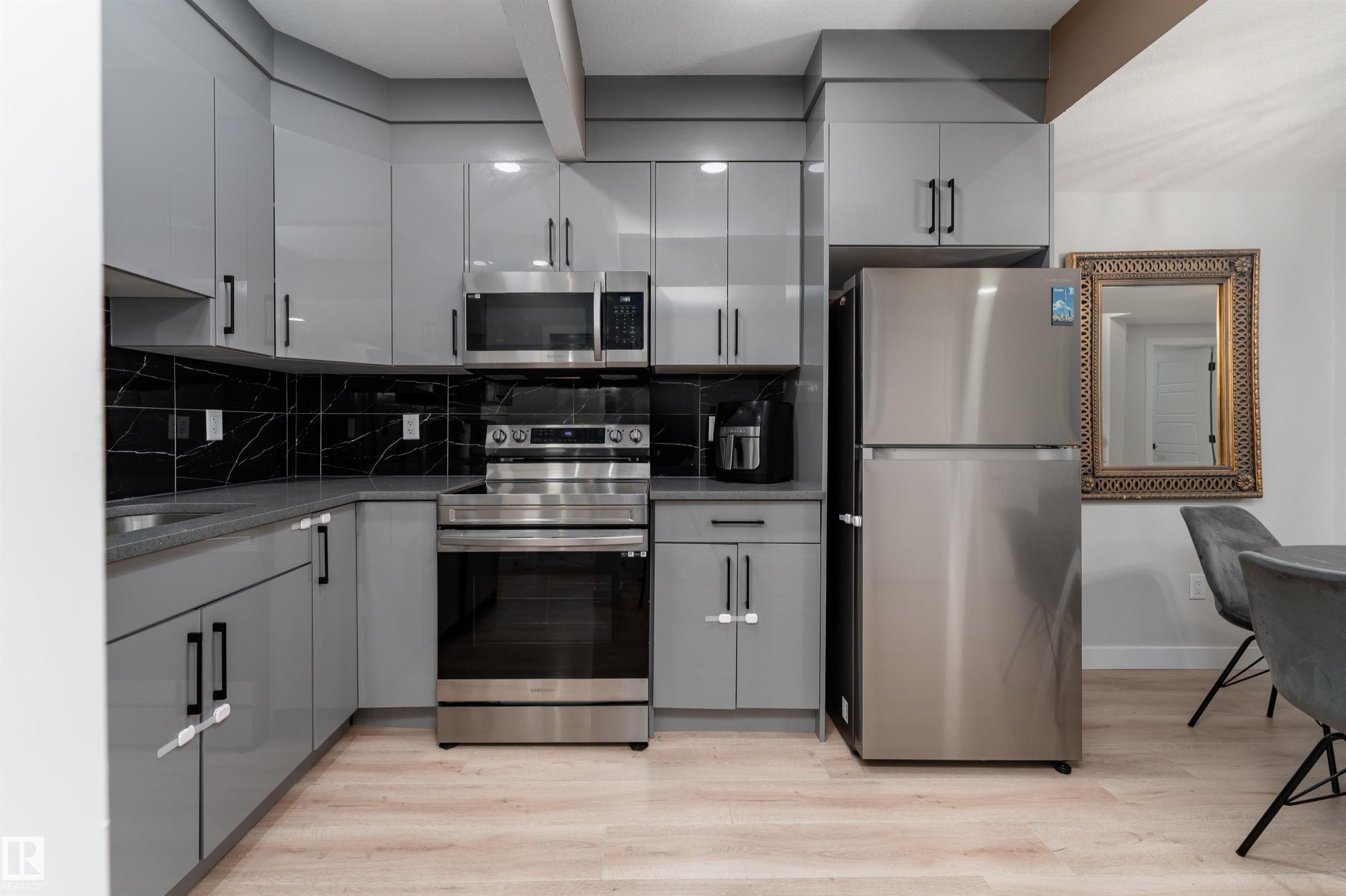 Modern kitchen featuring light grey cabinetry with black hardware, stainless steel appliances, and a black marble-style backsplash - 993 Berg Pl, Leduc, AB - Indoor Photo Showing Kitchen