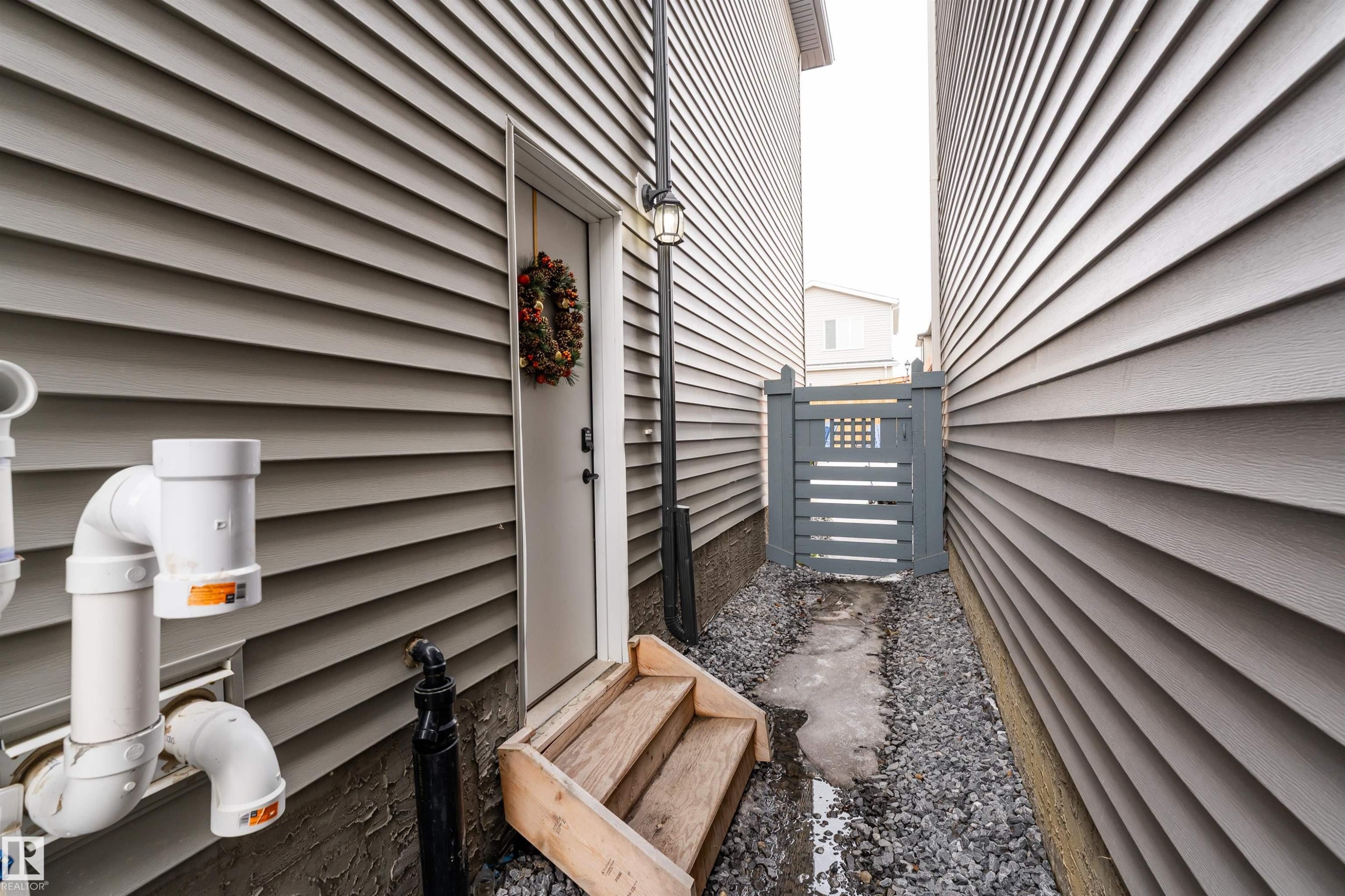 The property features gray siding, a white exterior door with wooden steps, and a gray gate in a gravel path - 993 Berg Pl, Leduc, AB - Outdoor