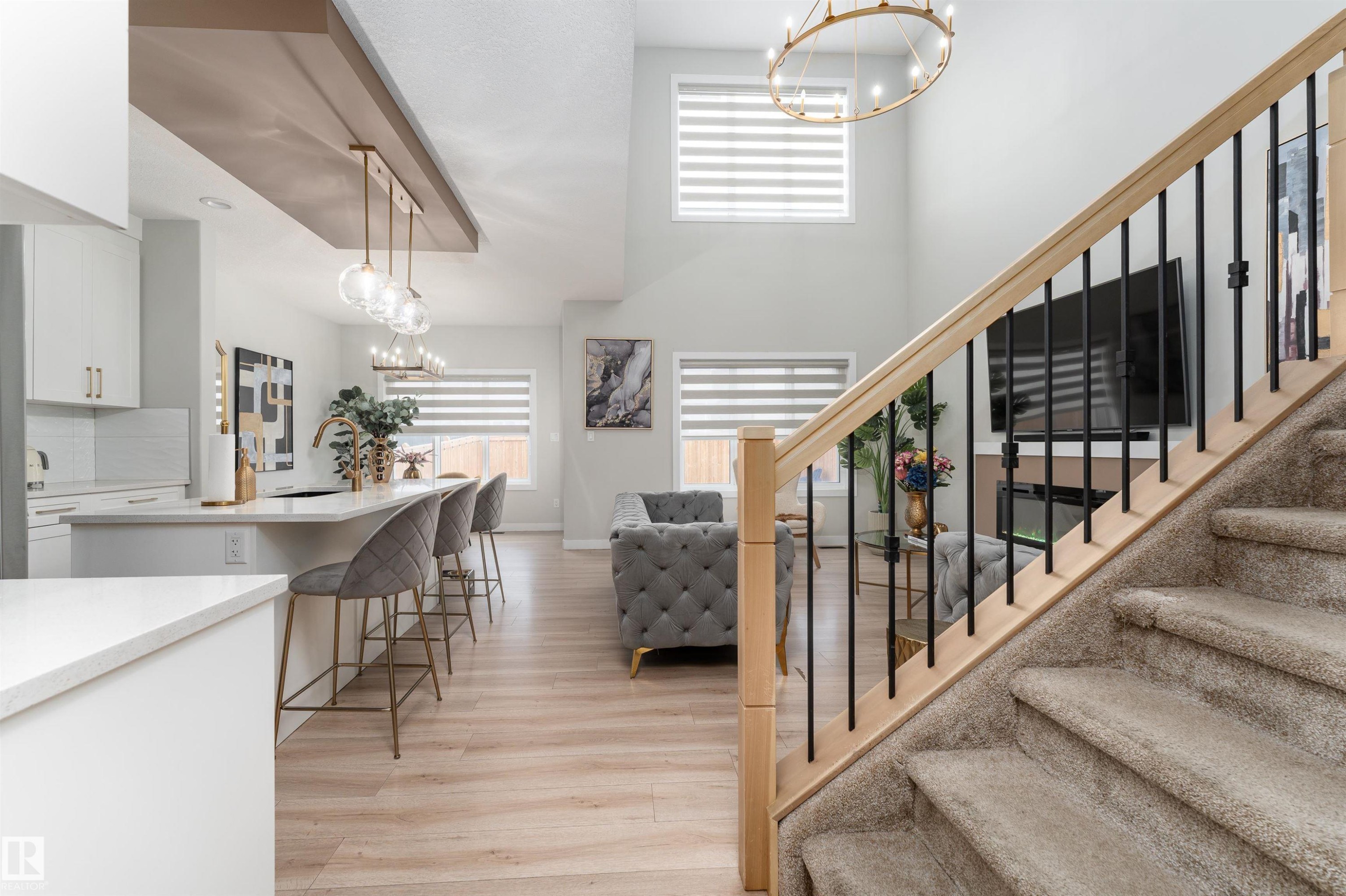 The property features an open-concept layout with light wood-style flooring, a kitchen island with seating, and a carpeted staircase with a light wood handrail and black balusters - 993 Berg Pl, Leduc, AB - Indoor Photo Showing Other Room