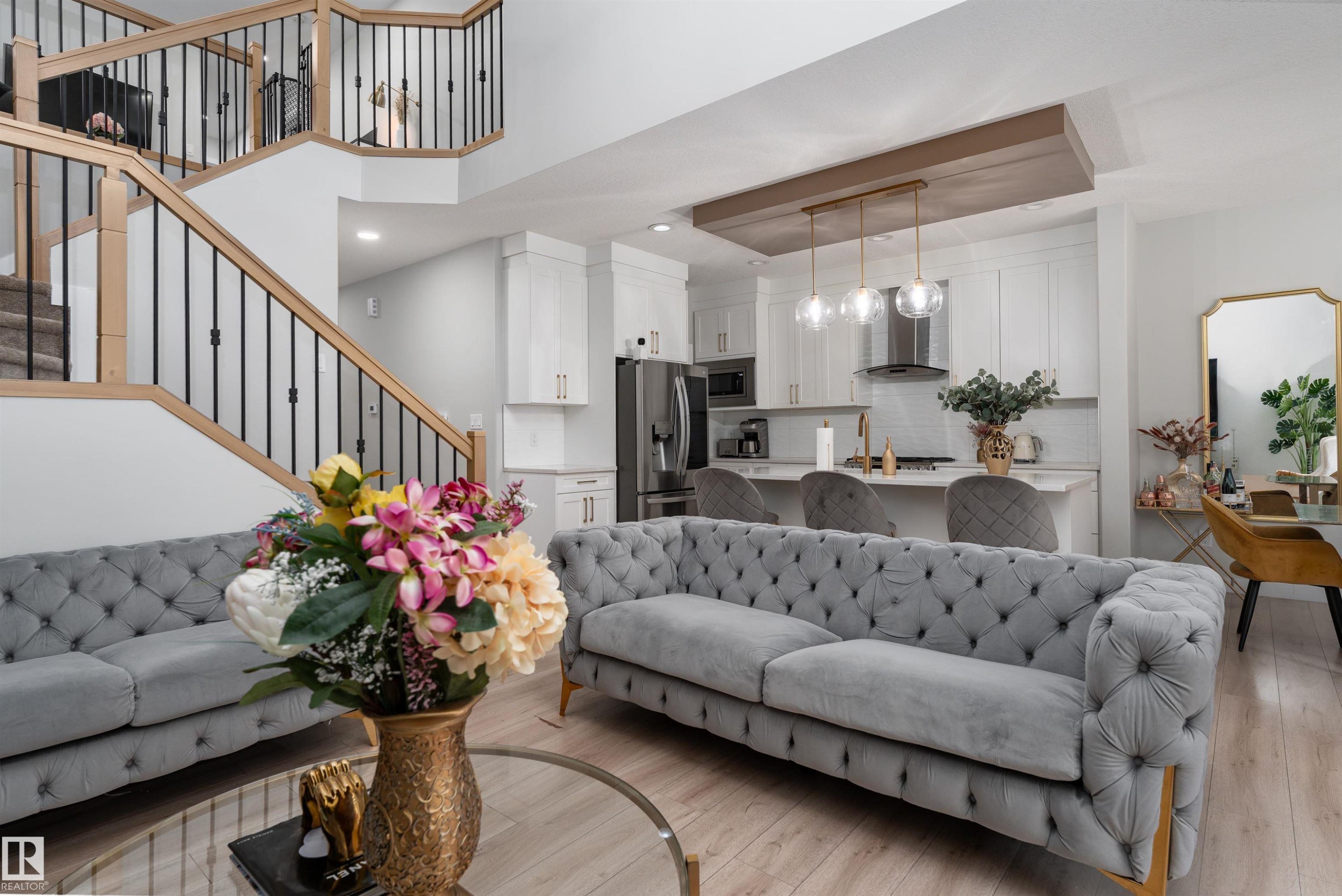 The property features an open-concept living area with light wood flooring, a modern kitchen with white cabinetry and stainless steel appliances, and a staircase with light wood handrails and black balusters - 993 Berg Pl, Leduc, AB - Indoor Photo Showing Living Room