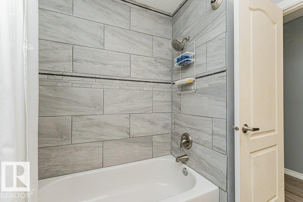 The bathroom features a bathtub with a tiled shower surround, including a decorative mosaic accent strip - 8 Duke Drive, Lamont, AB - Indoor Photo Showing Bathroom