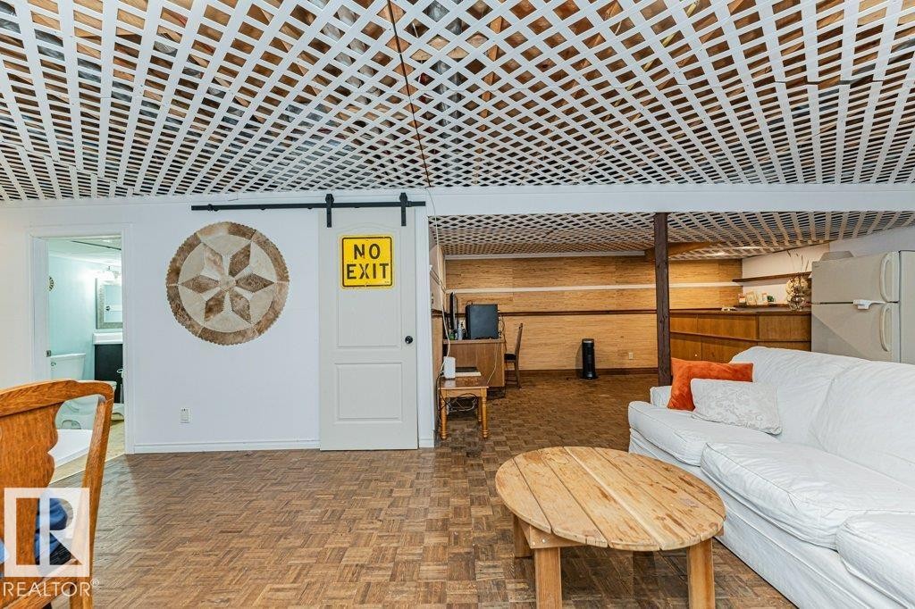 Spacious living area featuring a white lattice ceiling, wood parquet flooring, and a white sliding barn door - 8 Duke Drive, Lamont, AB - Indoor