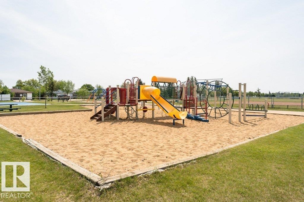 A community amenity featuring a sand area with a colorful playground structure, surrounded by a grassy lawn - 8 Duke Drive, Lamont, AB - Outdoor